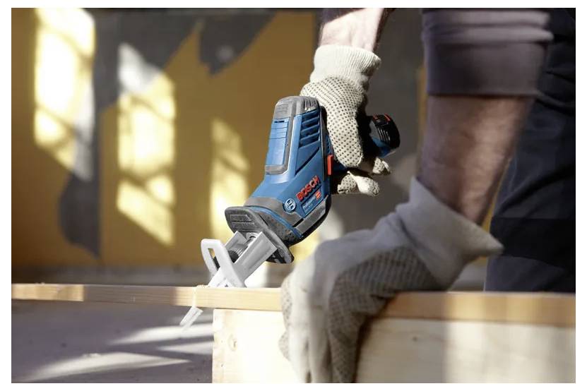 Eine Person mit Handschuhen bedient ein blaues und schwarzes Elektrowerkzeug auf einer Holzoberfläche in einer Werkstattumgebung.
