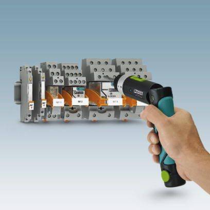 Eine Hand hält ein Infrarotthermometer, das auf eine Reihe von elektrischen Schaltern gerichtet ist, die in einem Schaltschrank installiert sind.