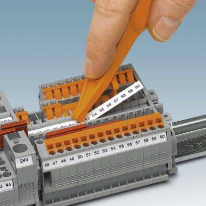 Eine Hand verwendet ein orangefarbenes Werkzeug, um Drähte an einem elektrischen Verteilerkasten anzuschließen.