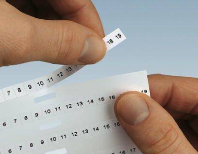 Zwei Hände ziehen nummerierte Etikettenstreifen mit Zahlen von 7 bis 18 ab.