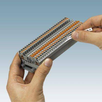 Person hält eine graue Klemmleiste mit orangefarbenen Hebeln, die zur elektrischen Verbindung von Leitern verwendet wird.