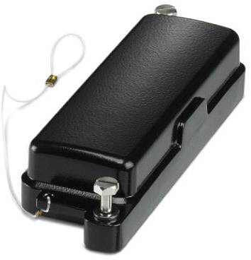 Ein schwarzes, rechteckiges Objekt mit zwei Schrauben oben und einer weißen Schnur, möglicherweise ein elektronisches Bauteil oder Gehäuse.