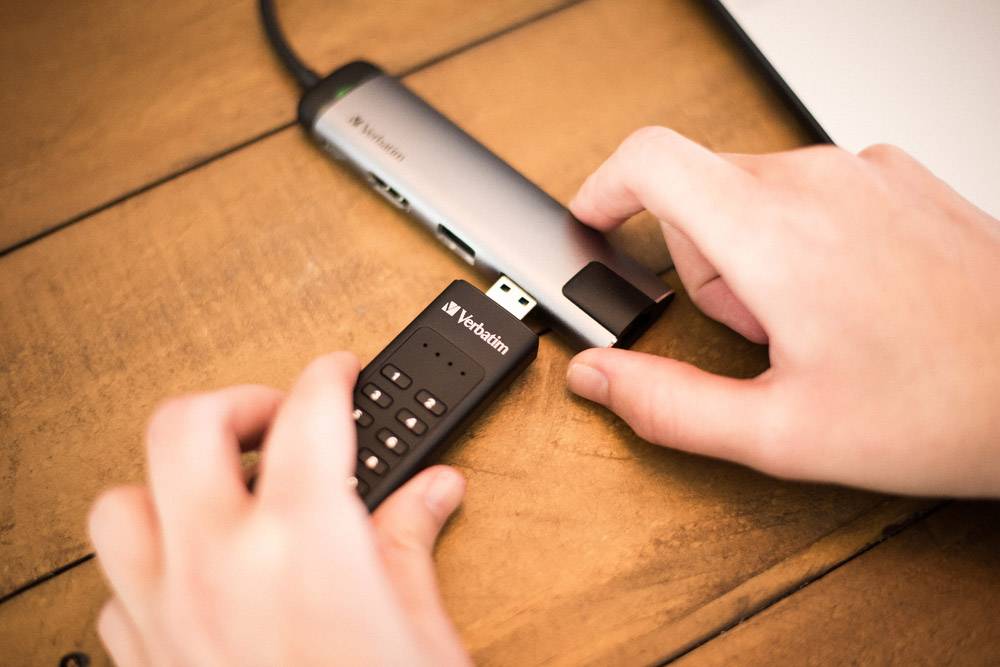Eine Hand verbindet ein Verbatim USB-Laufwerk mit einem USB-Hub auf einem Holztisch.