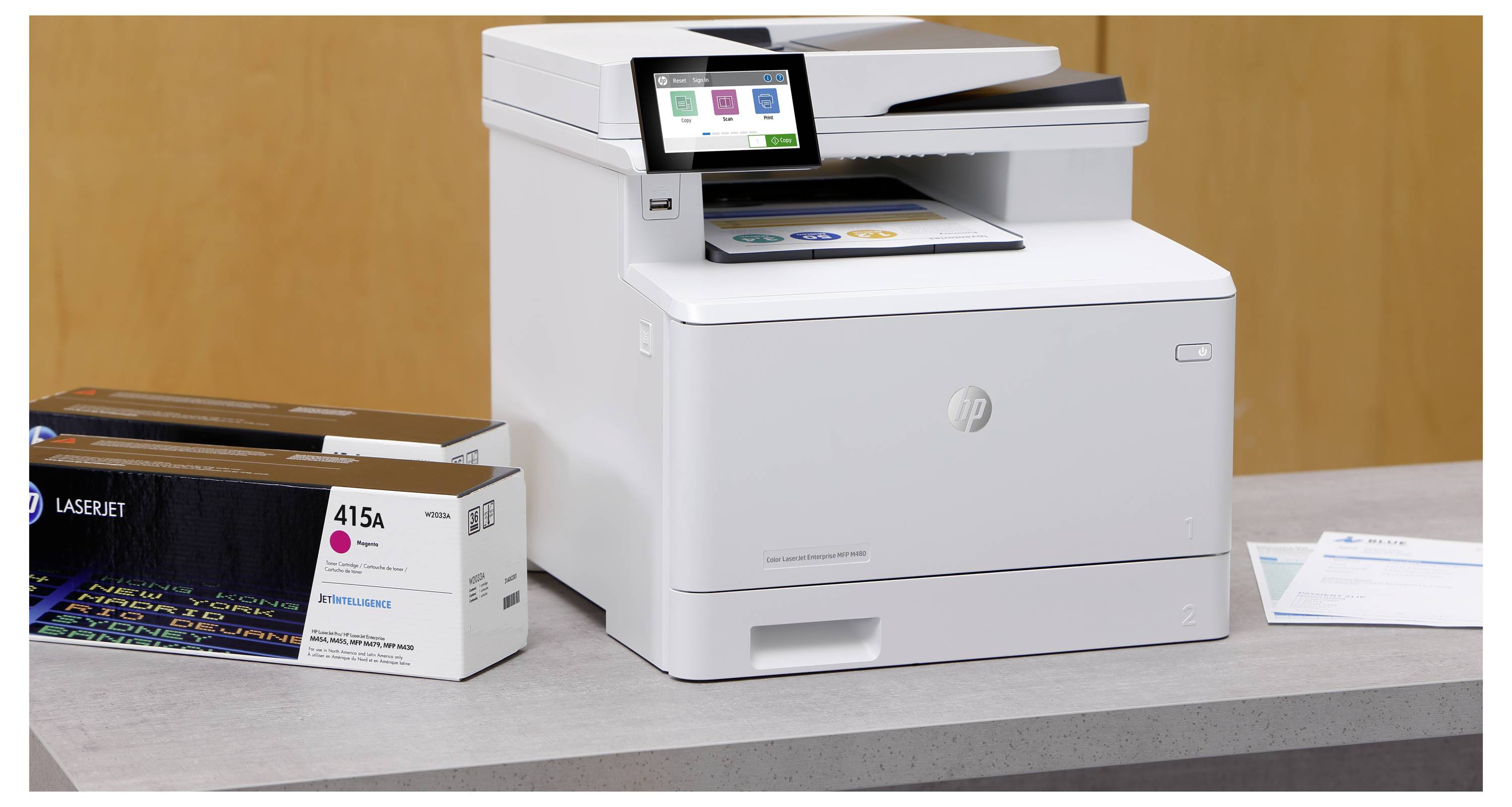Weißer HP LaserJet-Drucker auf einer Arbeitsplatte neben einer Tonerbox mit der Bezeichnung „415A" und einem Ausgabefach mit bedrucktem Papier.