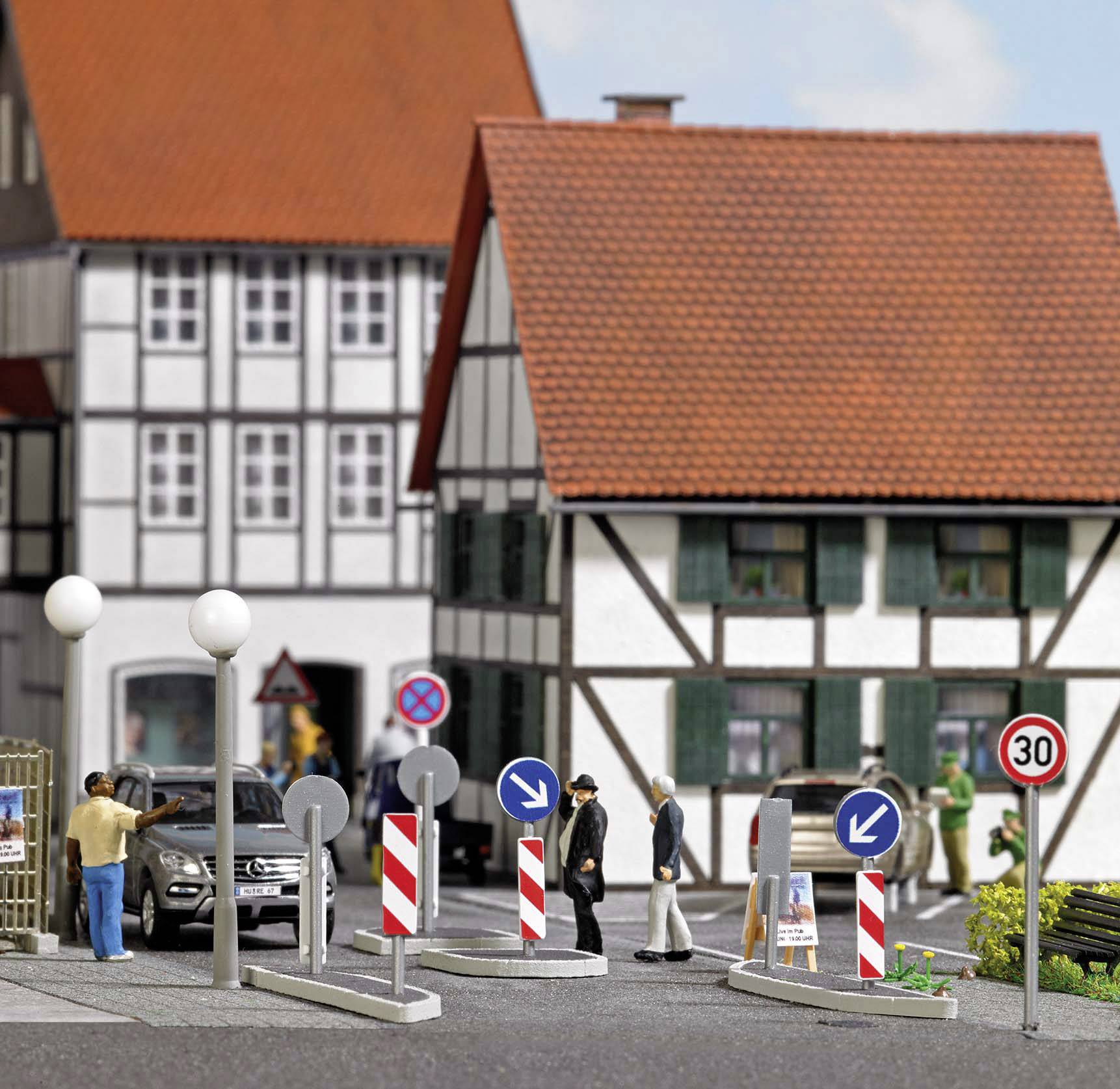 Miniaturdorf mit Fachwerkhäusern, Parkverbotsschildern und Autos an einer Straßenkreuzung. Menschen gehen auf dem Gehweg.