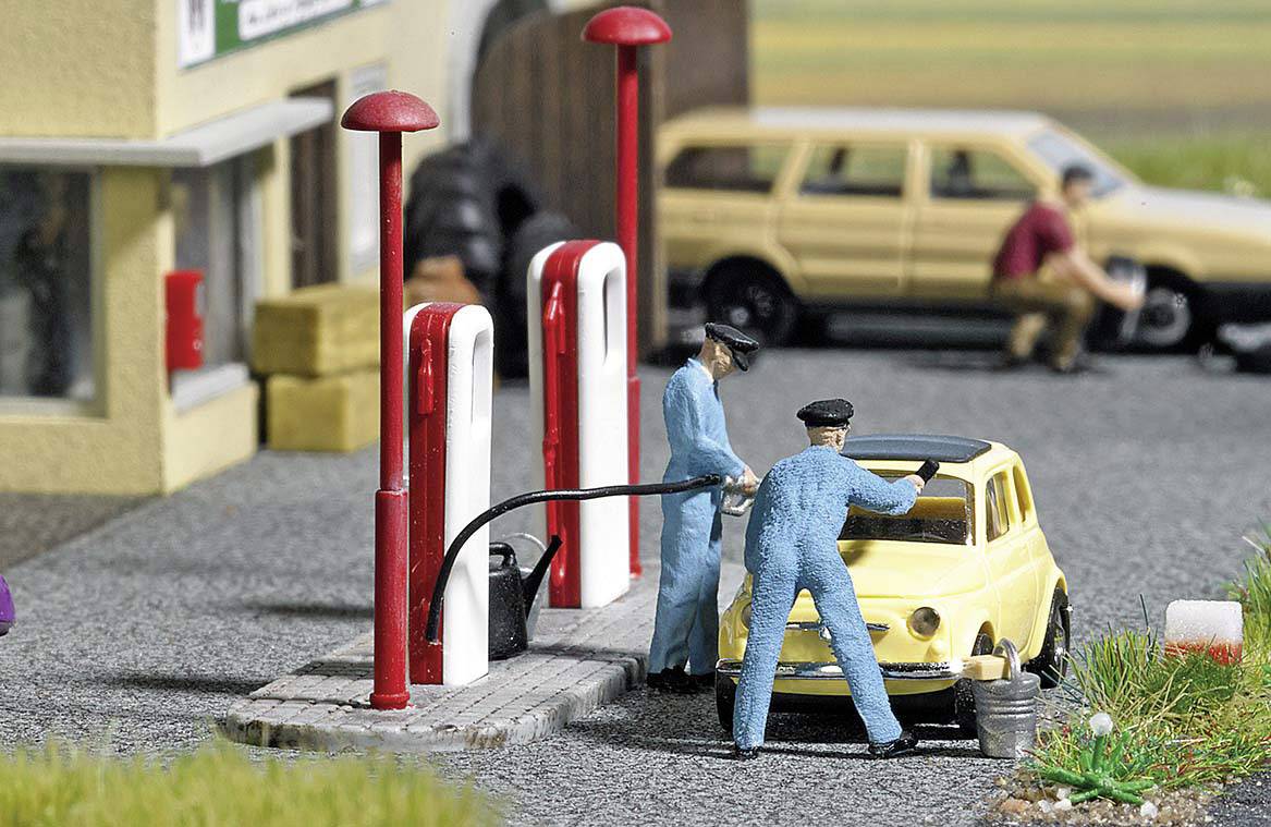 Zwei Miniaturfiguren tanken ein gelbes Auto an einer Tankstelle. Im Hintergrund ist ein weiteres Fahrzeug mit einer Person erkennbar.