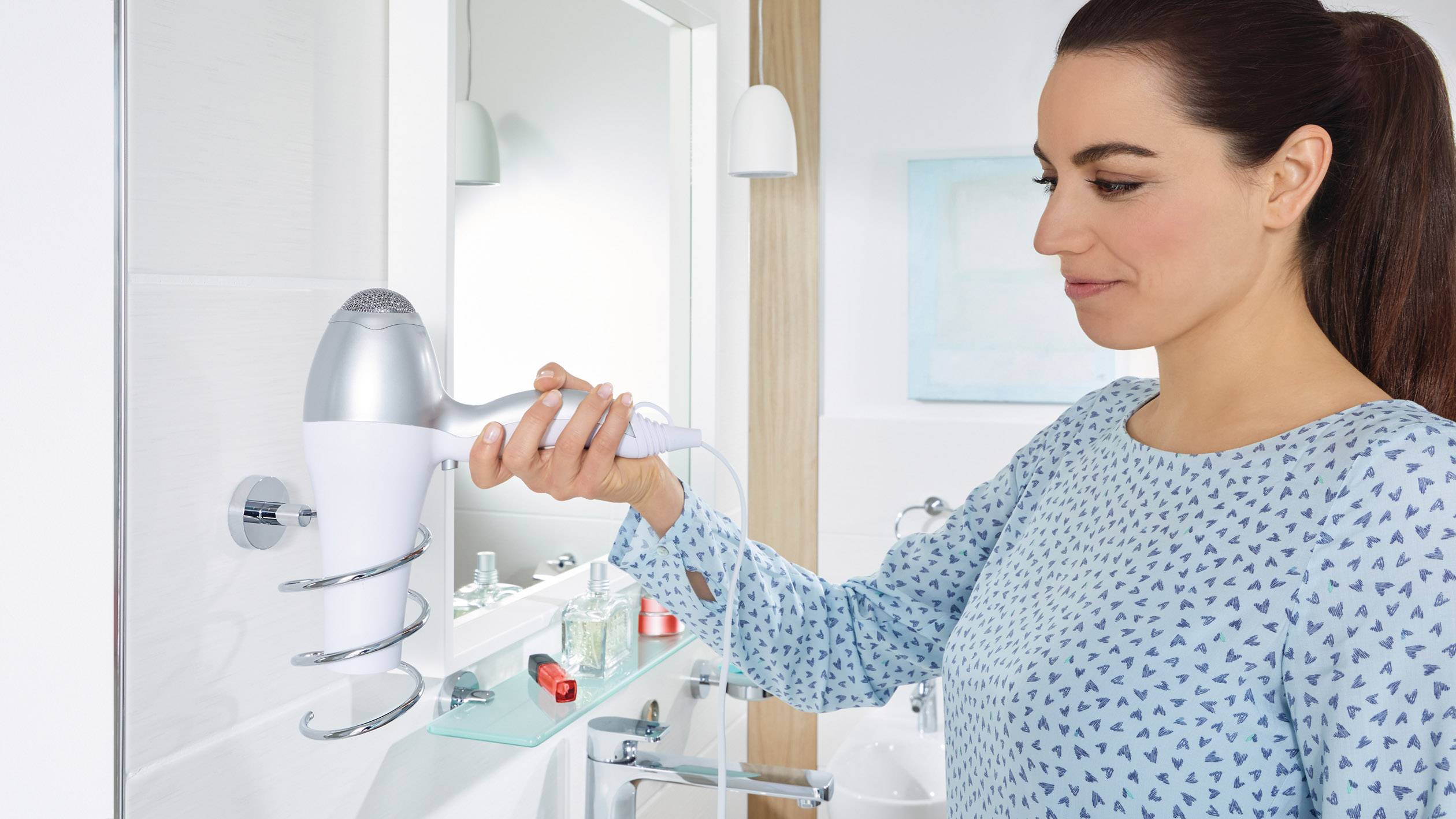 Eine Frau verwendet einen weißen Haartrockner in einem Badezimmer mit modernem Design. Sie steht vor einem Spiegel und trocknet sich die Haare.