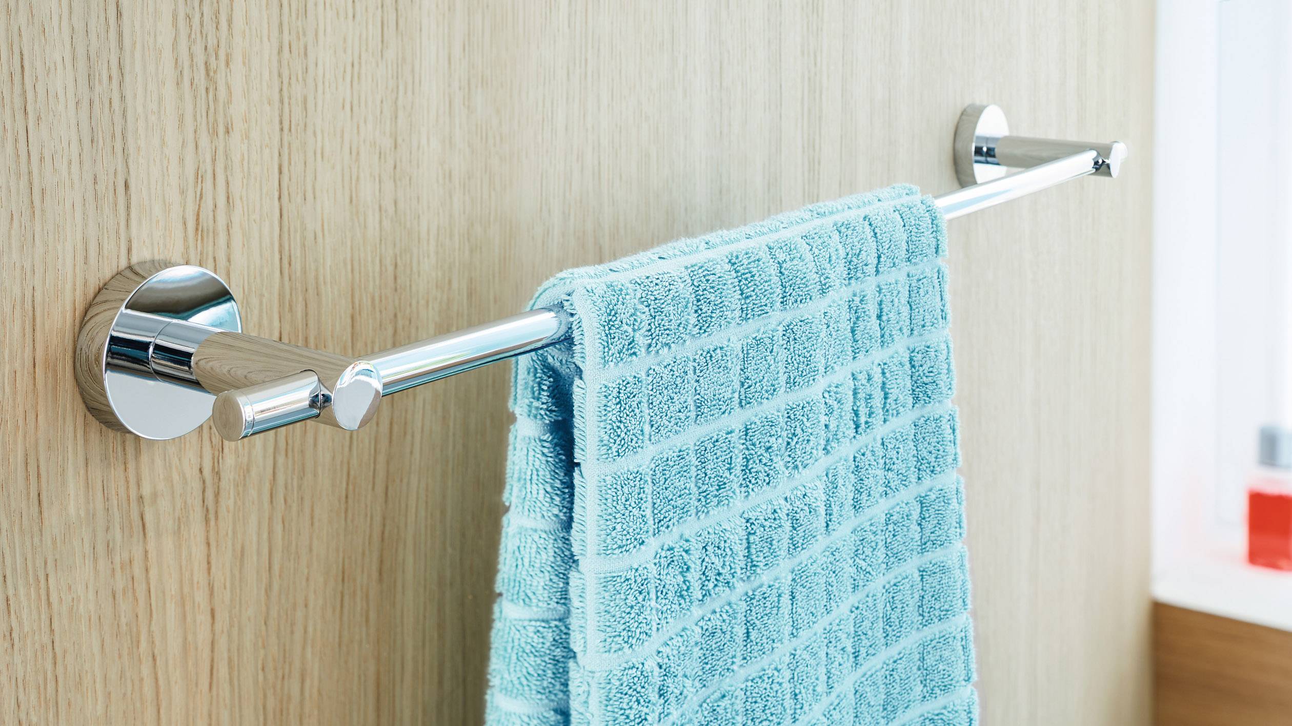 Ein türkisfarbenes Handtuch hängt an einem glänzenden Handtuchhalter an einer Holzwand in einem Badezimmer.