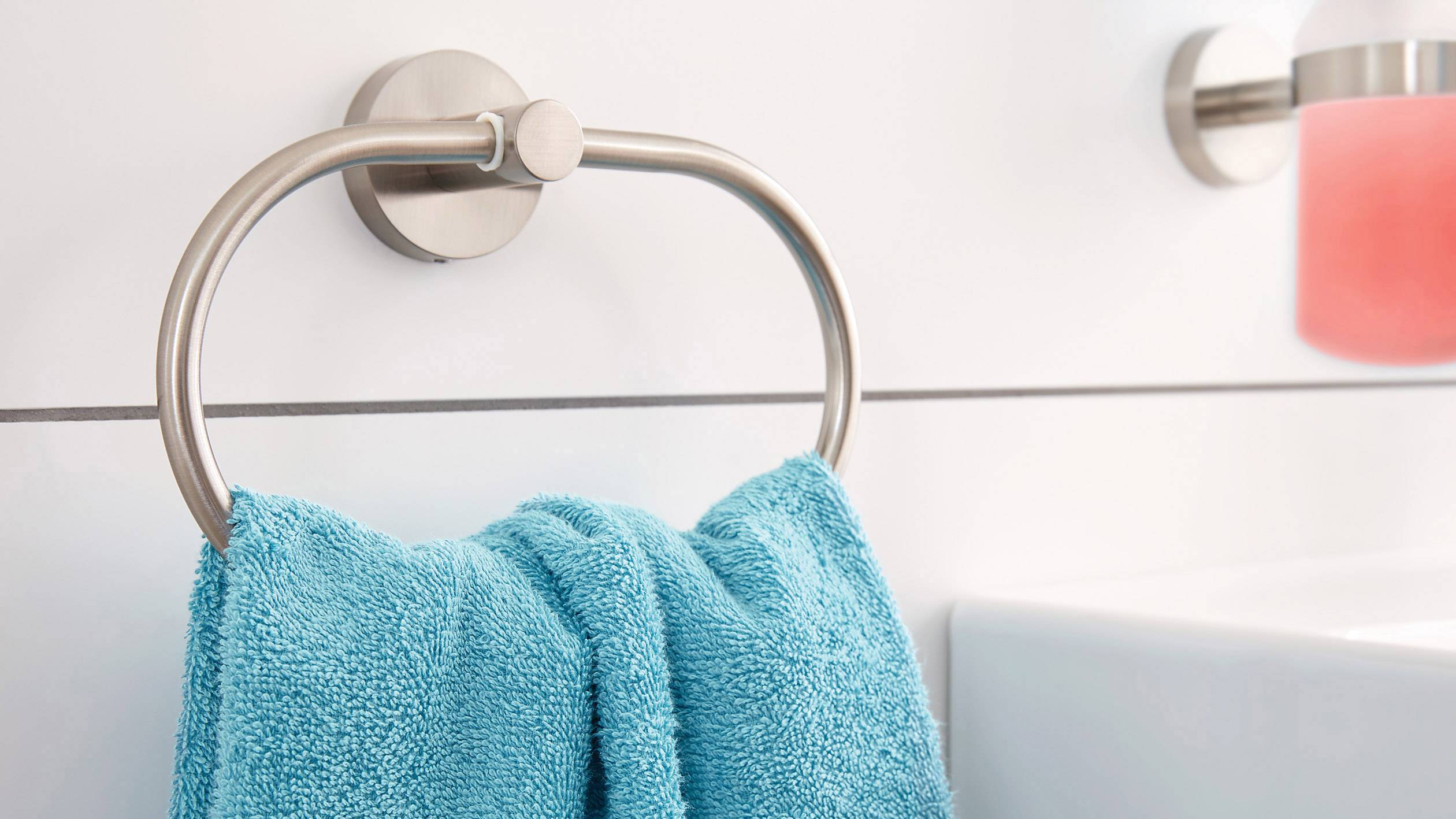 Ein blaues Handtuch hängt an einem runden, silbernen Handtuchhalter an einer weißen Badezimmerwand.