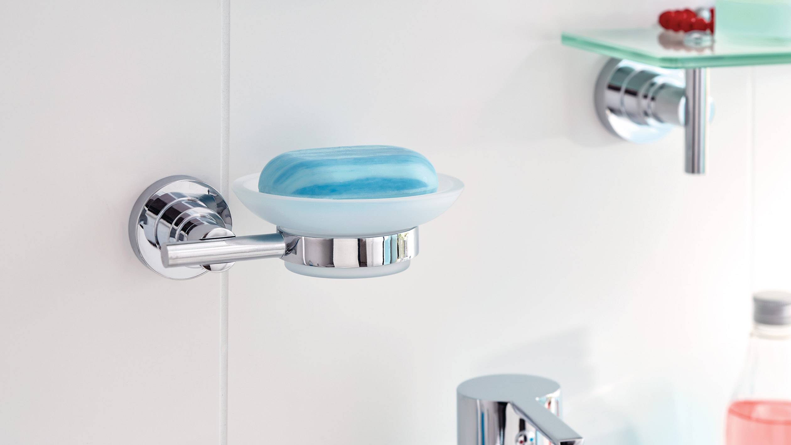 Eine blaue Seife liegt in einer runden, wandmontierten Seifenschale aus Metall und Glas im Badezimmer.