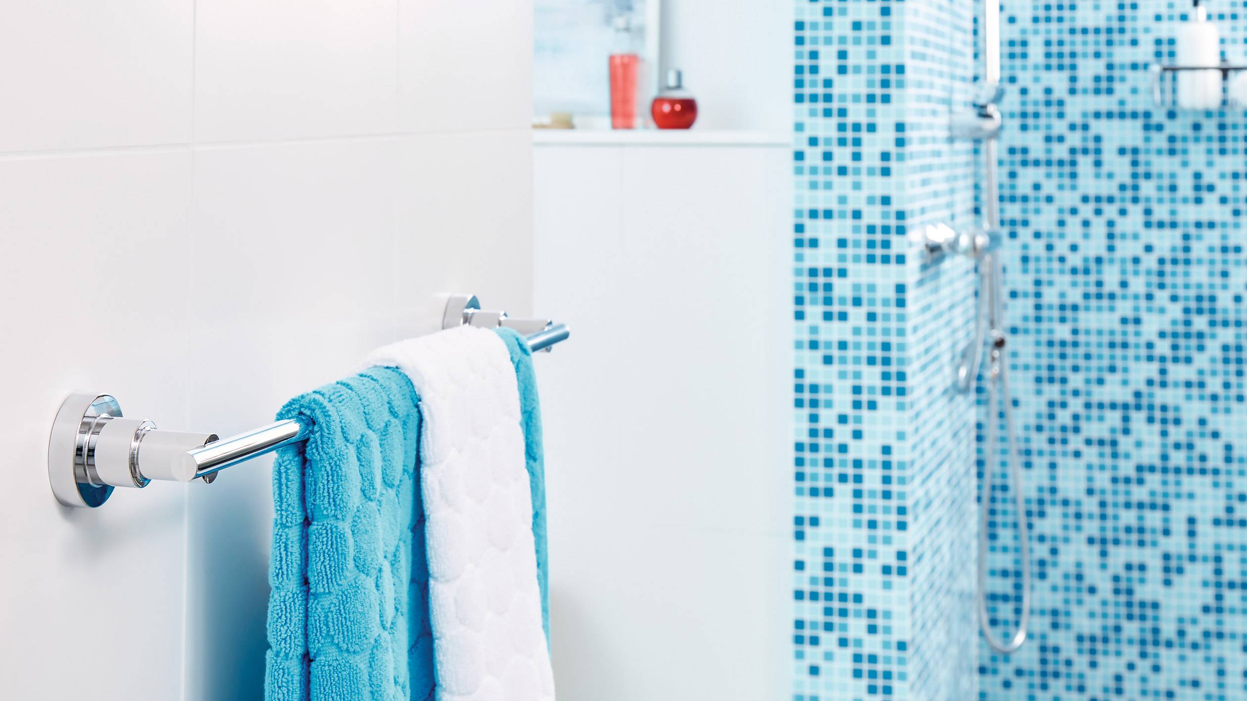 Ein Badezimmer mit blauen Mosaikfliesen an der Wand. Ein Handtuchhalter trägt ein blaues Handtuch. Eine Dusche ist sichtbar.