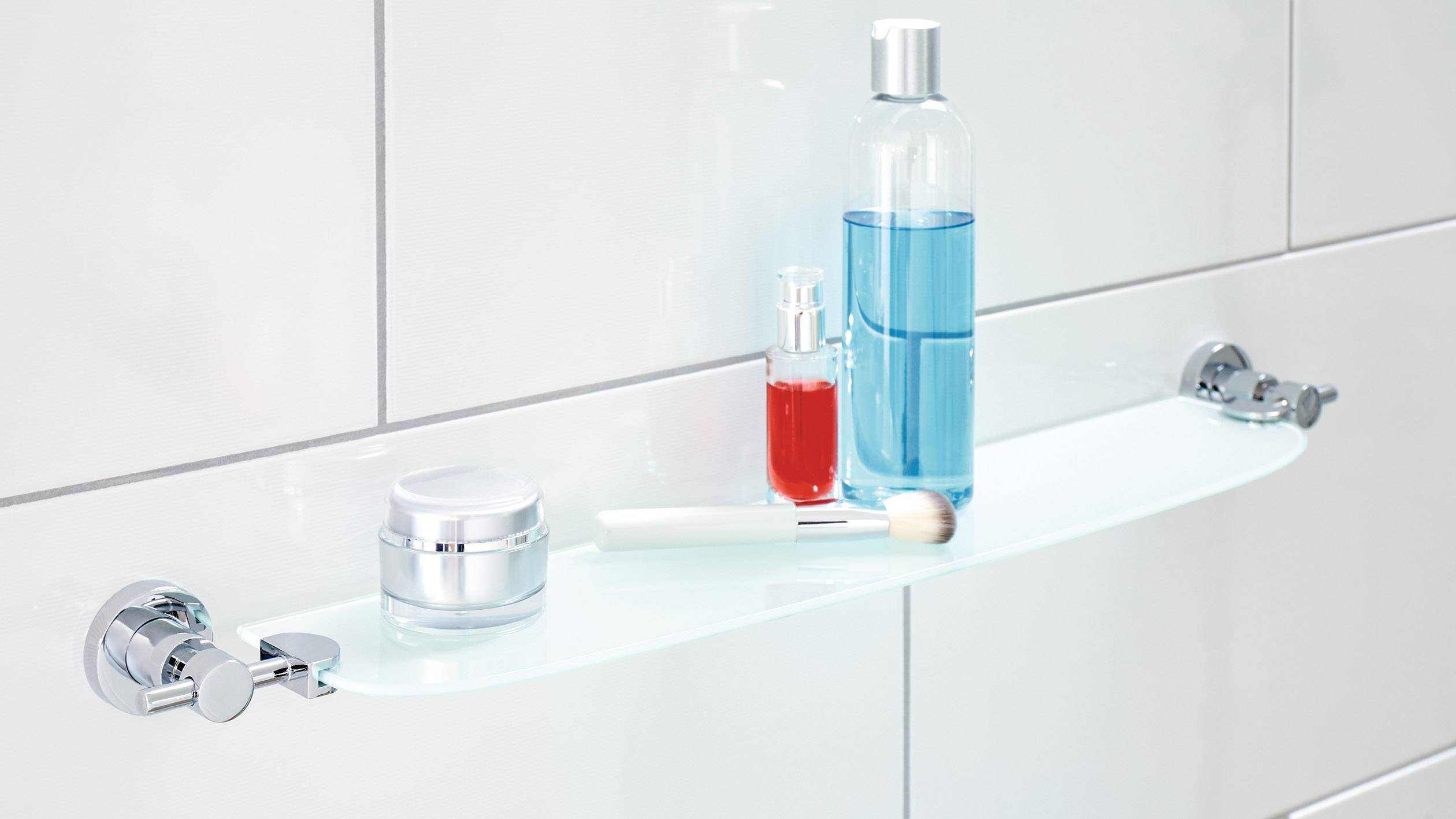 Glasregal im Badezimmer mit Hautpflegeprodukten: Eine blaue Flasche, rote Flasche, eine Creme und ein weißer Pinsel sind sichtbar.