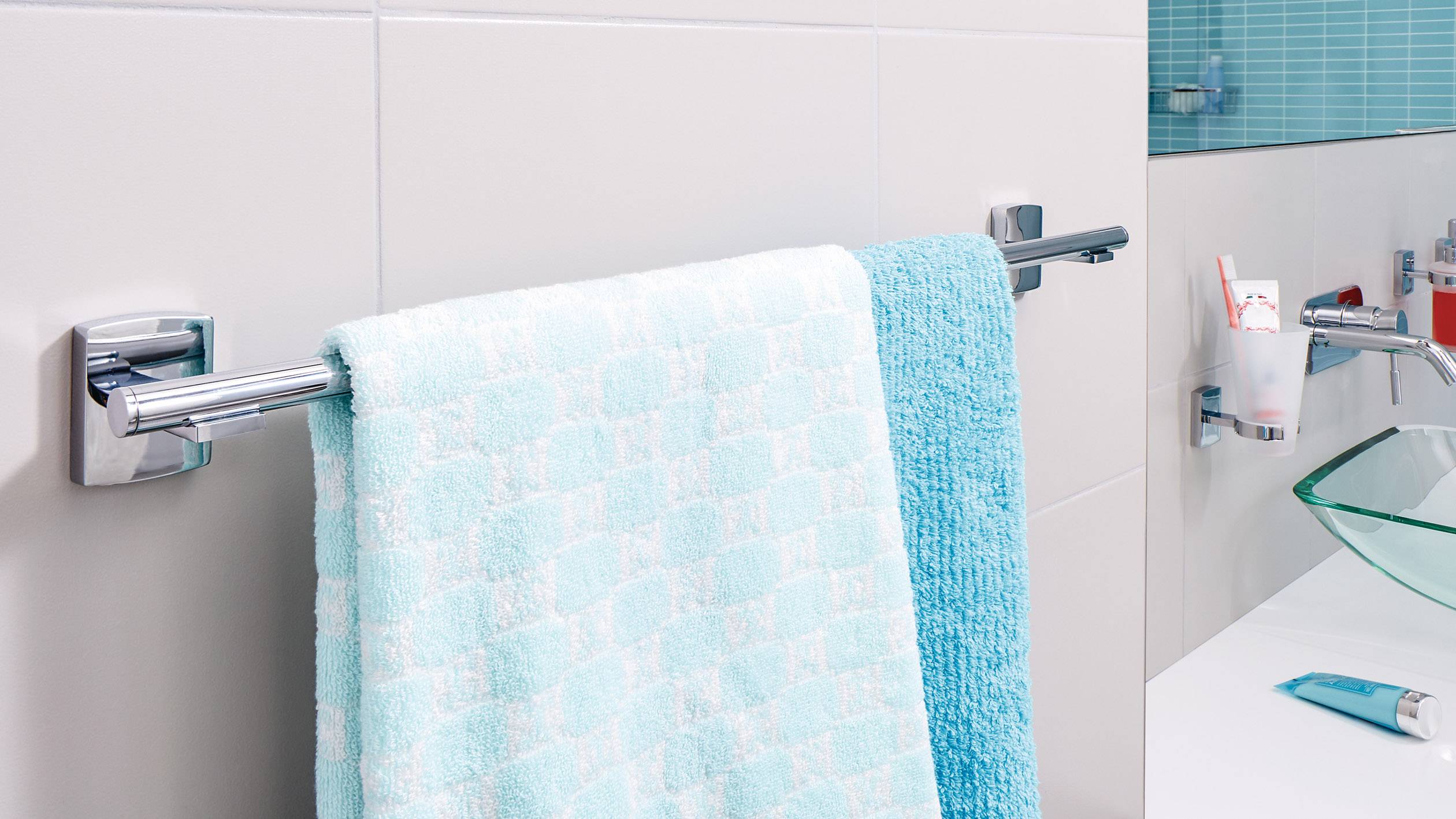 Zwei blaue Handtücher hängen an einem Handtuchhalter im Badezimmer, neben einem Glaswaschbecken und einer Zahnbürste.