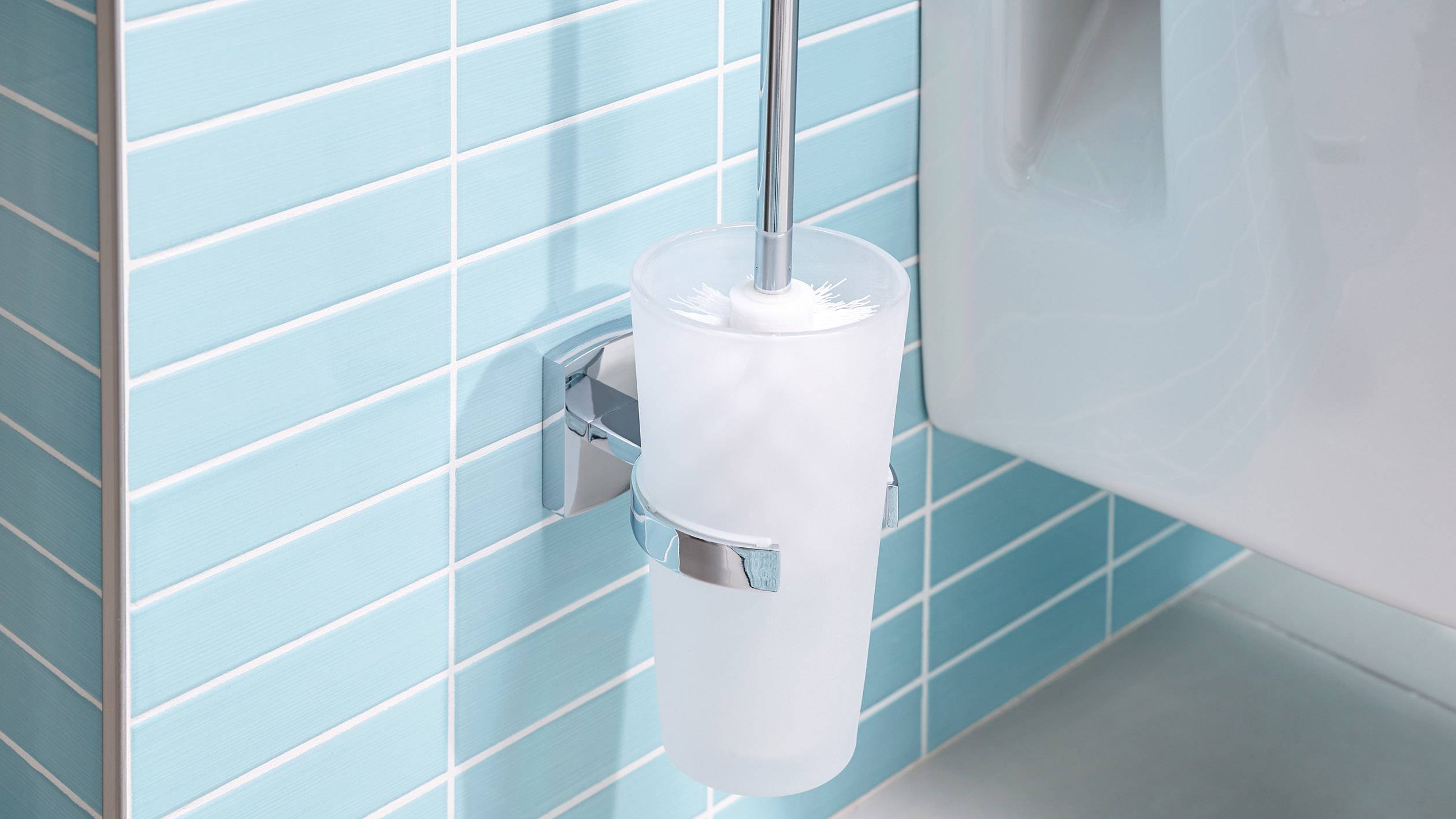 Eine Toilettenbürste in einem Halter an einer blauen gefliesten Badezimmerwand neben einer weißen Toilette.