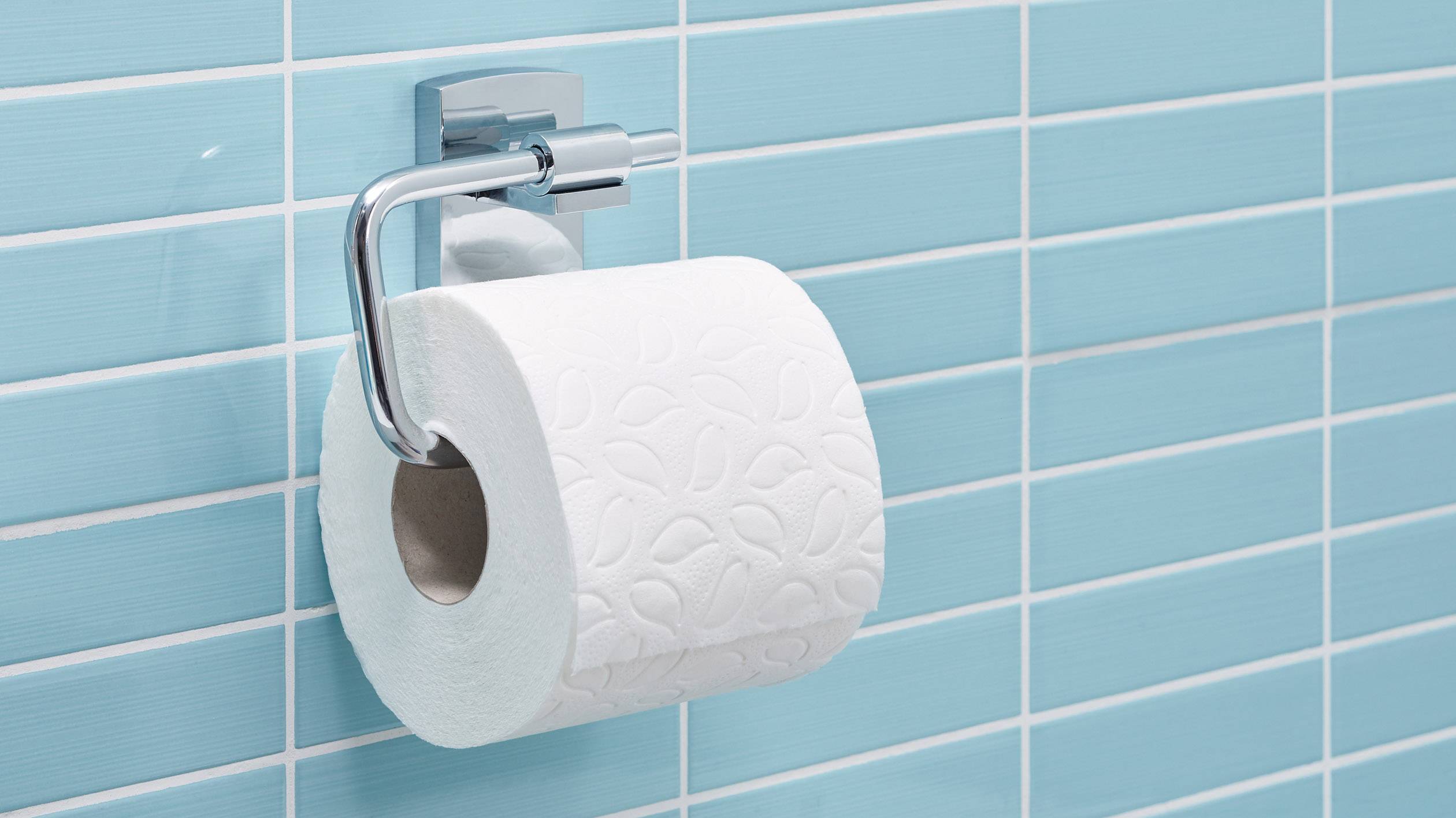 Toilettenpapierrolle hängt an einem Wandhalter vor einer blau gefliesten Wand.