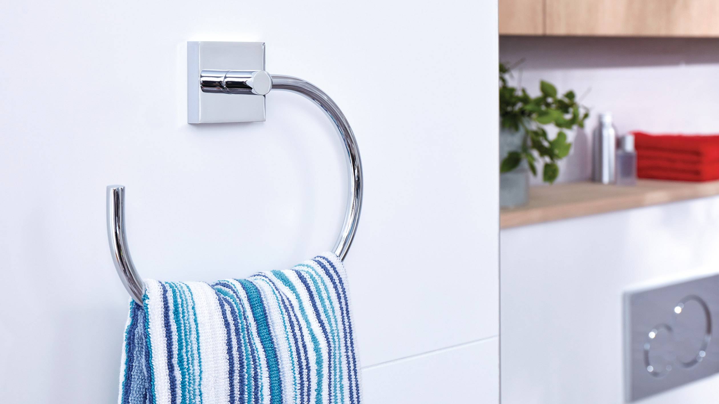 Ein gestreiftes Handtuch hängt an einem runden, verchromten Handtuchhalter im Badezimmer. Im Hintergrund sind rote Handtücher.