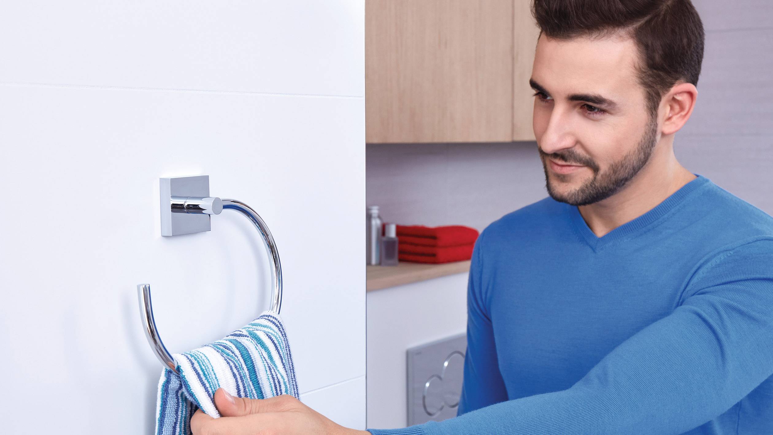 Ein Mann hängt ein blau-weiß gestreiftes Handtuch an einen Handtuchhalter im Badezimmer.