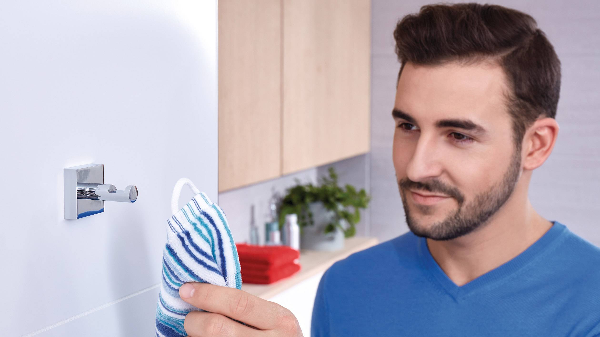 Mann hängt ein blau-weiß gestreiftes Handtuch an eine Hakenleiste im Badezimmer.
