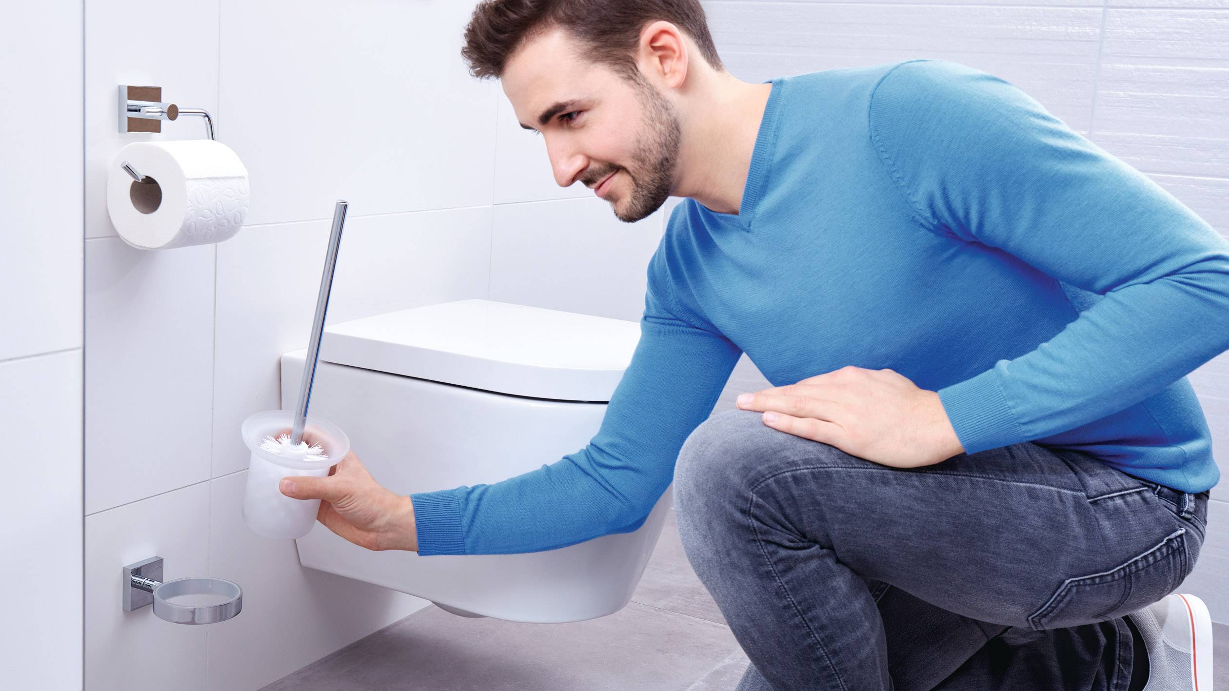 Ein Mann in blauer Kleidung reinigt eine Toilettenschüssel mit einer Bürste in einem modernen Badezimmer.