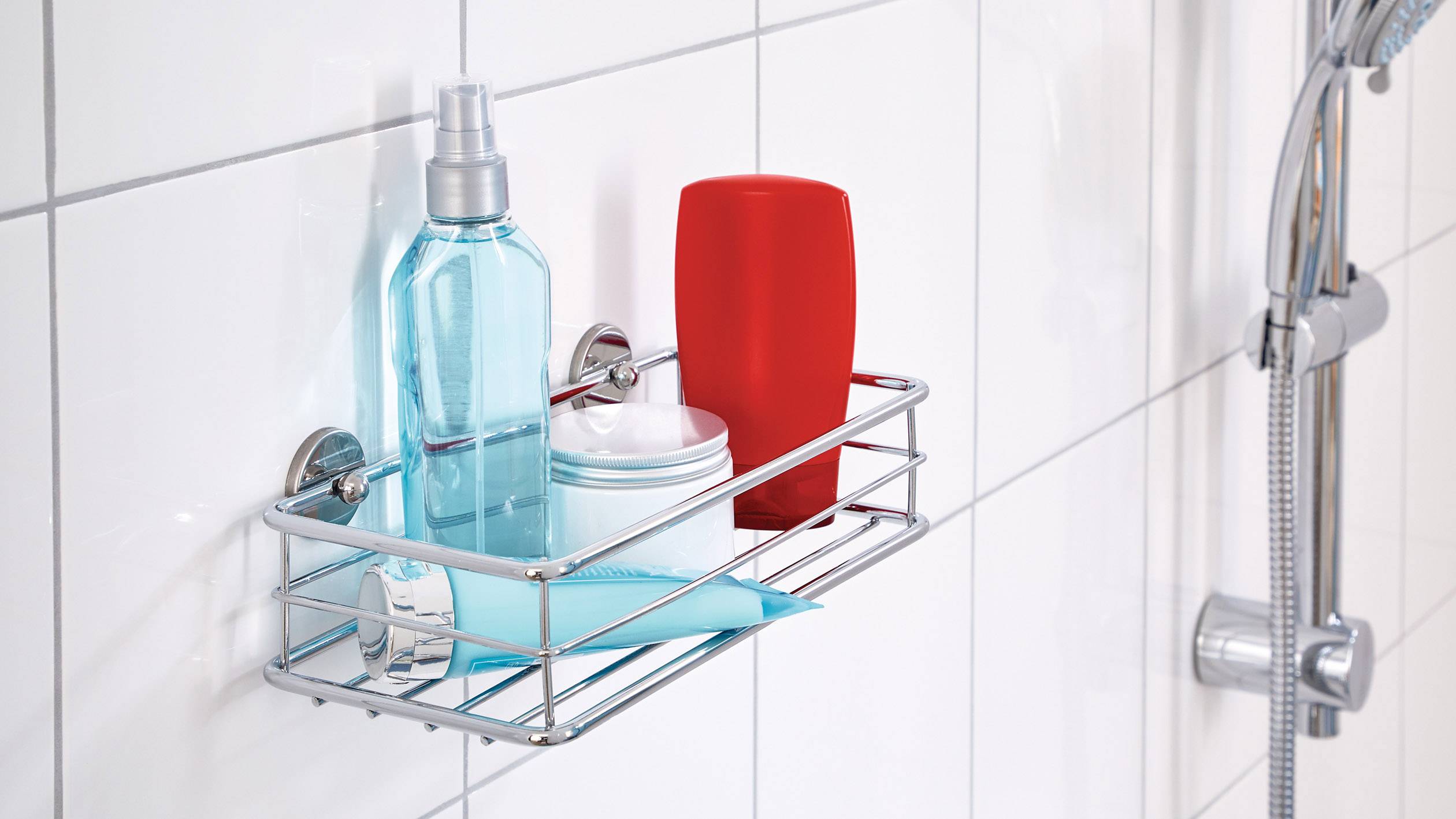 Duschablage an der Wand mit verschiedenen Pflegeprodukten: eine blaue Sprühflasche, eine rote Flasche und ein kleines rundes Behältnis.