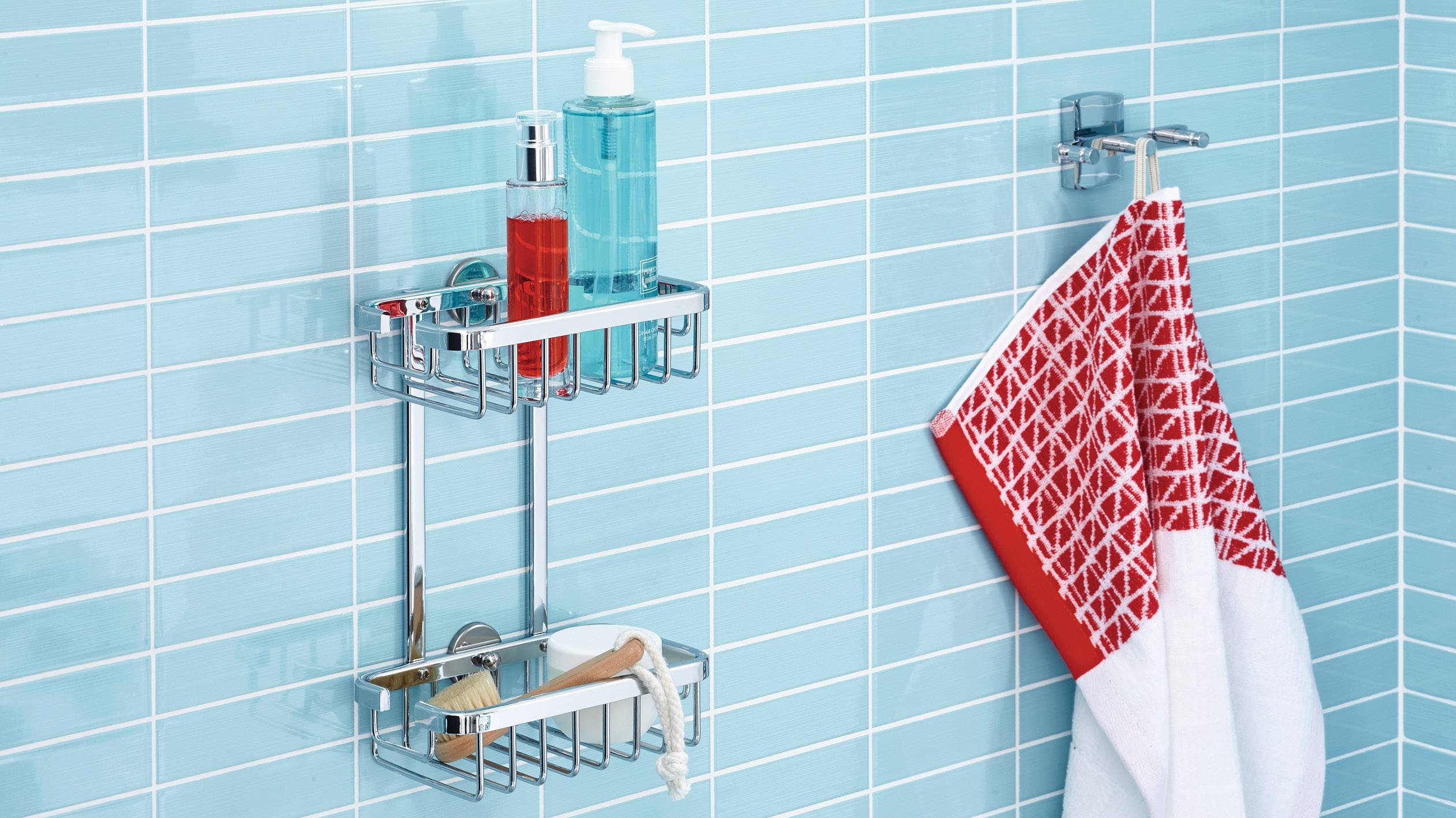 Ein Badezimmerregal aus Metall mit Hygieneartikeln wie Seifenflaschen und Bürsten ist an einer blau gefliesten Wand befestigt. Daneben hängt ein rot-weißes Handtuch.