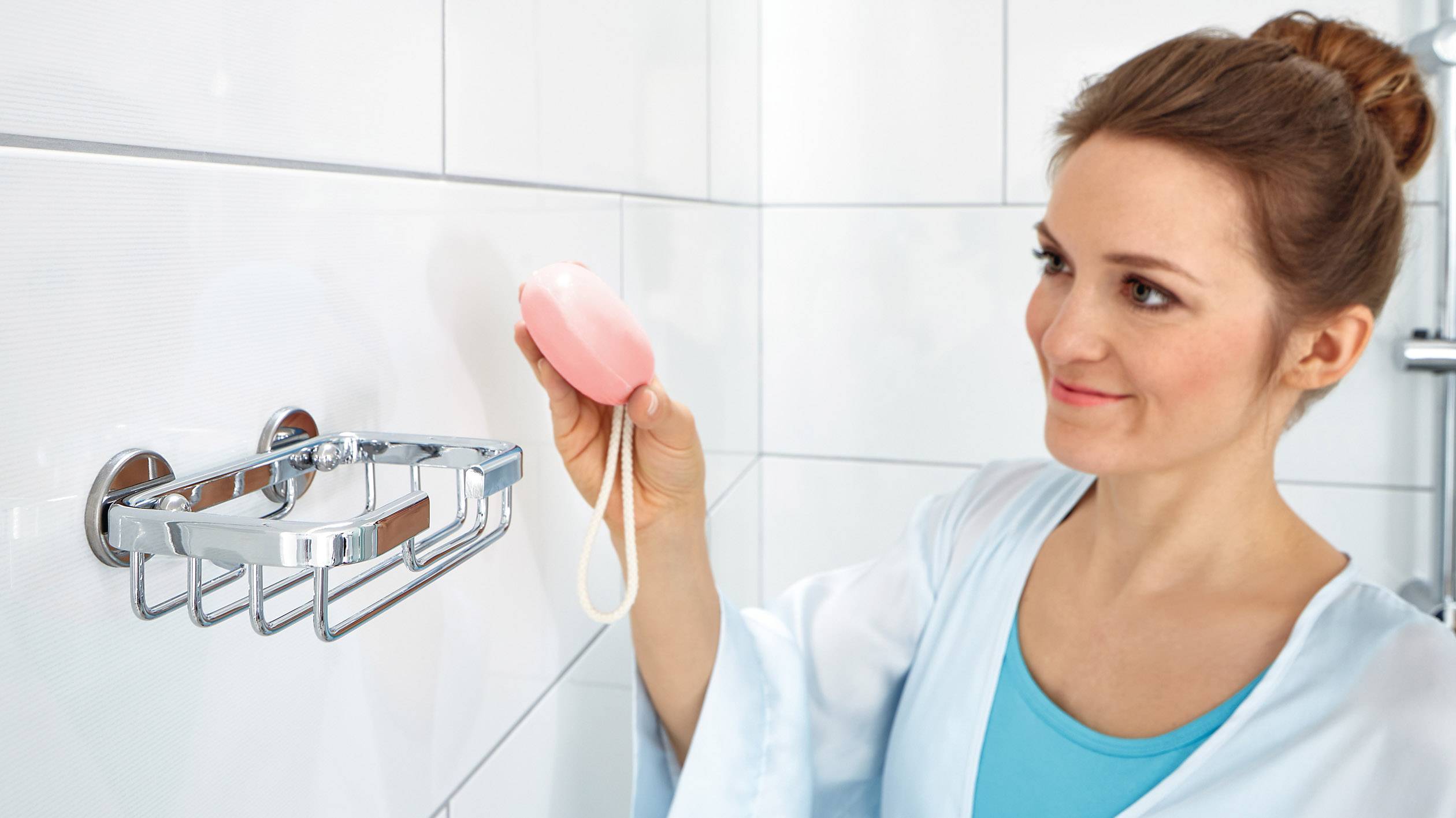 Eine Frau im Bademantel hängt ein Stück Seife in einem Halter in ihrem Badezimmer auf, um Ordnung zu schaffen.