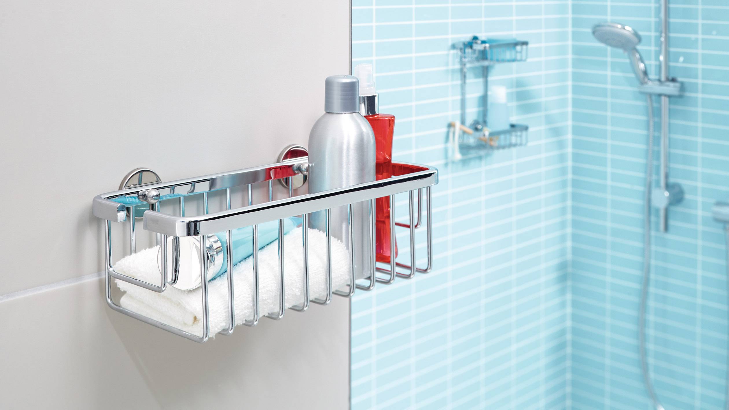 Ein Duschkorb aus Metall an einer gefliesten Wand, mit Shampoo-Flaschen und einem Handtuch in einem modernen Badezimmer.