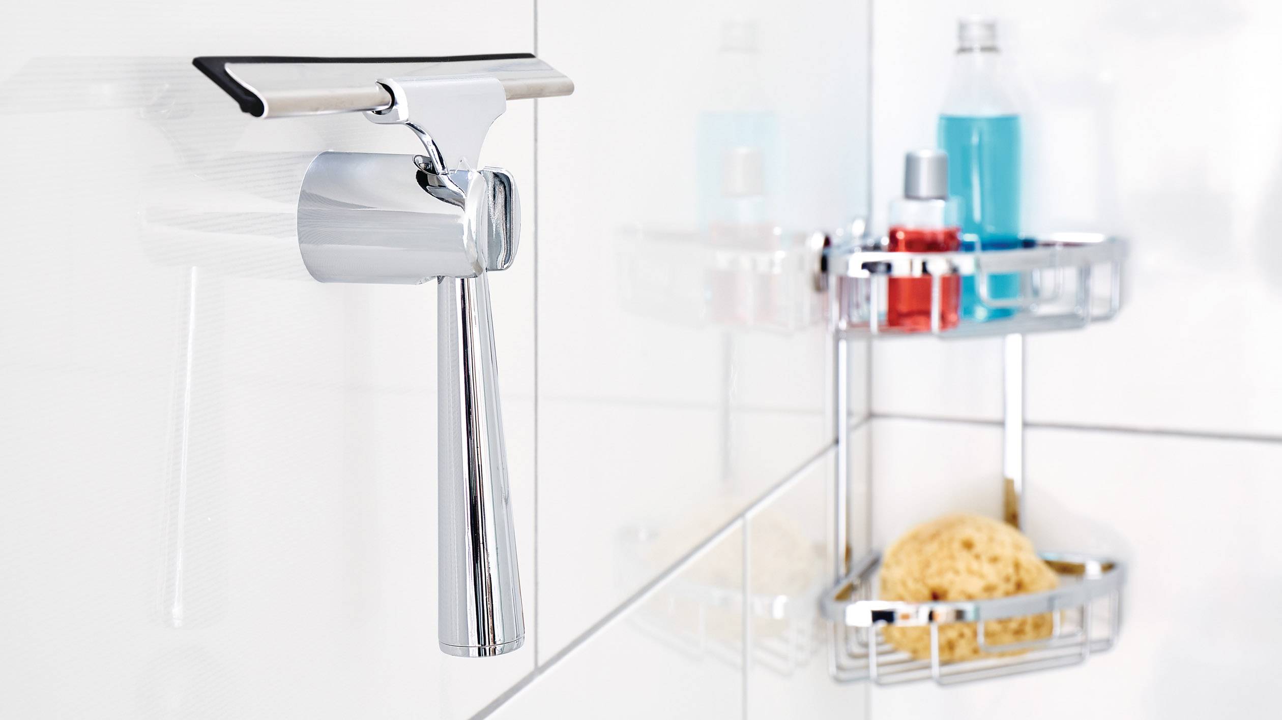 Chromgriffe an einer weißen Badezimmerwand, daneben ein Regal mit Pflegeprodukten und Schwamm, spiegeln moderne, saubere Einrichtung wider.