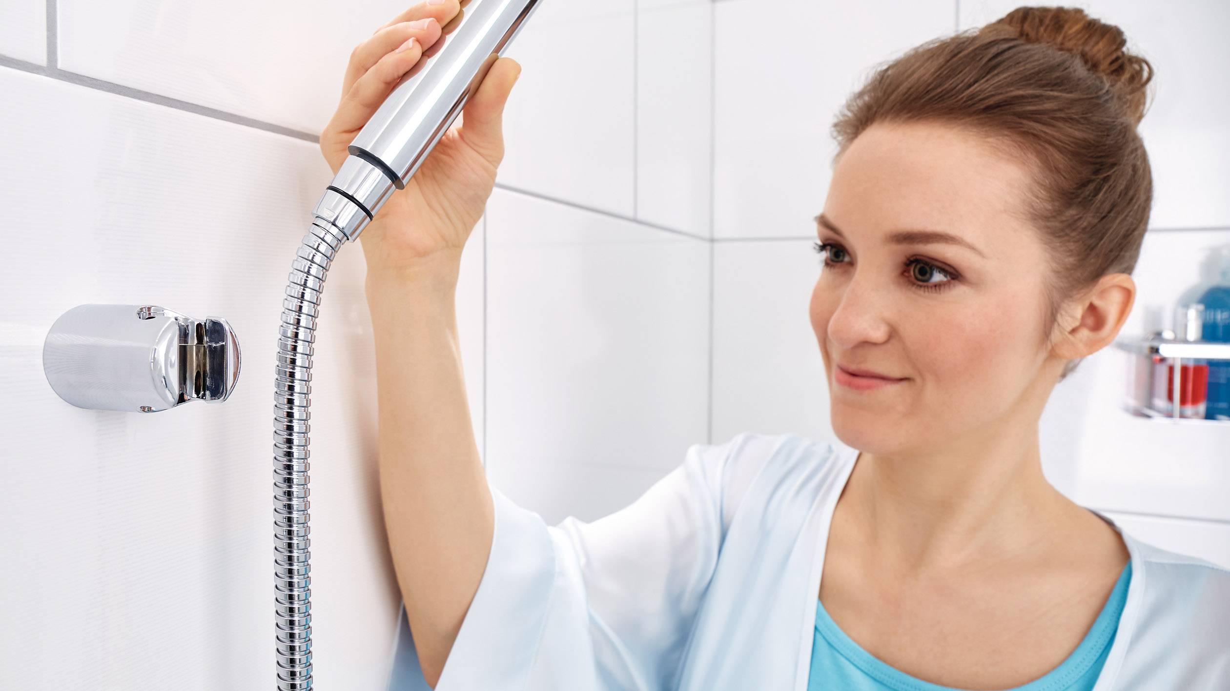 Eine Frau richtet einen Duschkopf in einem hellen Badezimmer aus. Sie trägt einen blauen Bademantel und wirkt konzentriert.