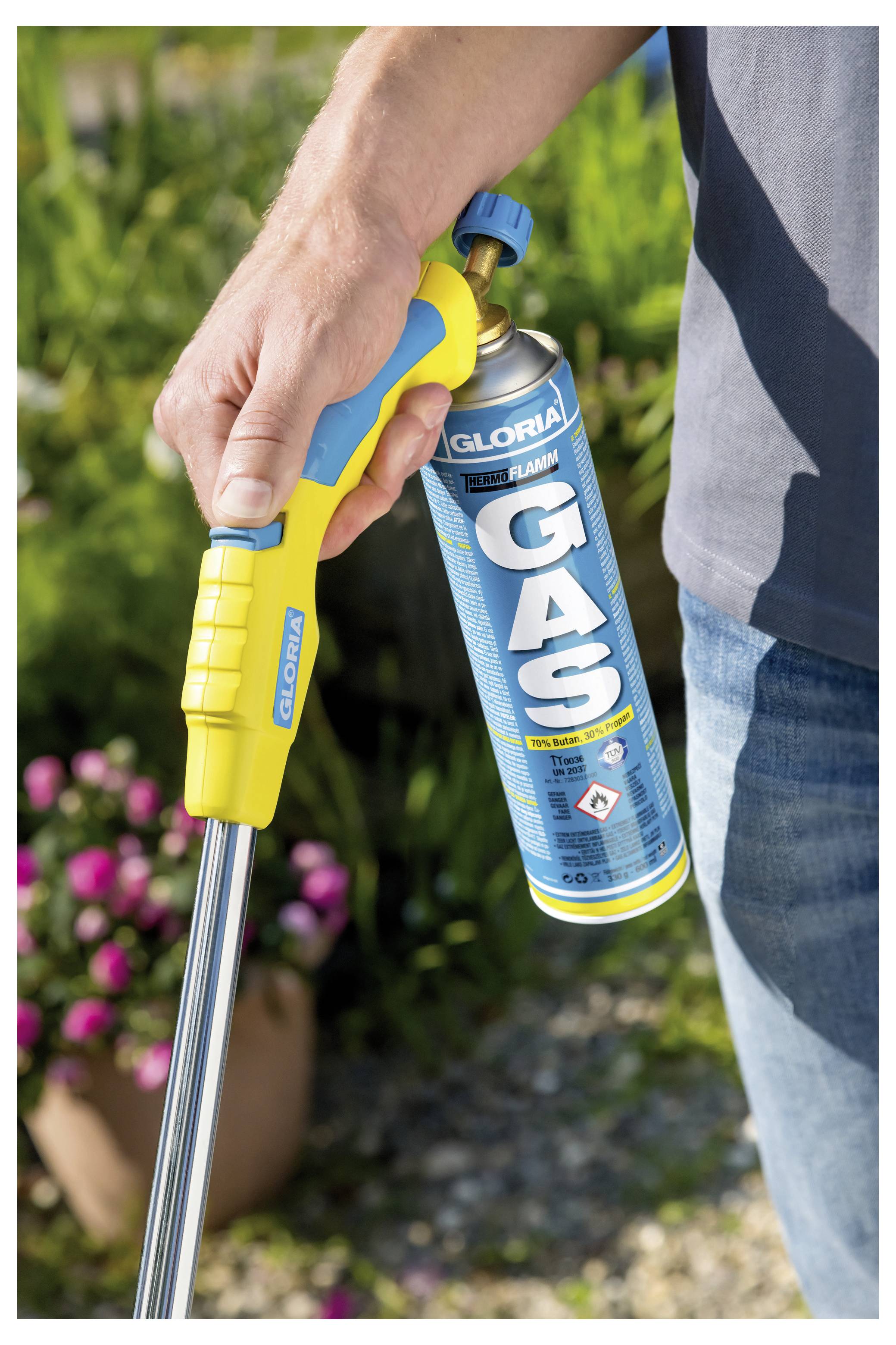 Eine Person hält eine GLORIA GAS-Sprühflasche mit einer langen Düse und verwendet sie draußen in einem Garten.