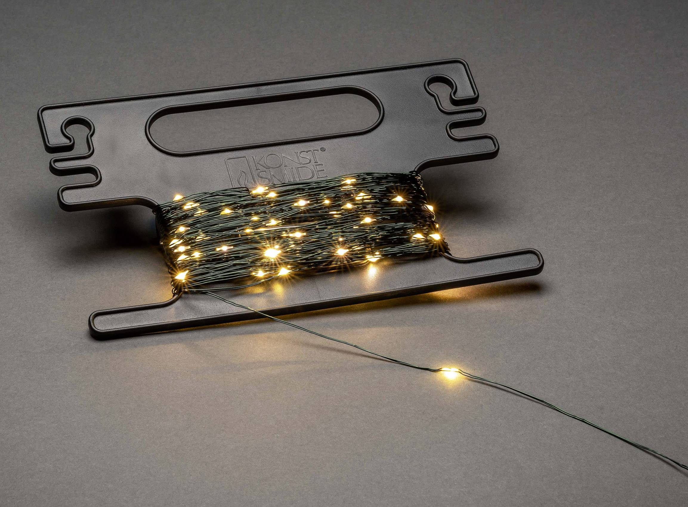 Eine Lichterkette mit kleinen, leuchtenden gelben LED-Lichtern ist auf einem schwarzen Kunststoffspuler aufgewickelt.
