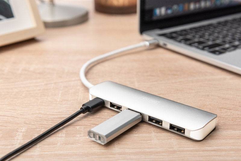 Ein Laptop ist über einen USB-C-Hub mit mehreren USB-Sticks verbunden, die auf einem Holztisch liegen.