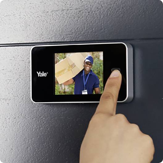 Eine Person legt seinen Finger auf einen Fingerabdruckscanner an einer Tür. Ein Display zeigt ein Bild mit einem Paketlieferanten.