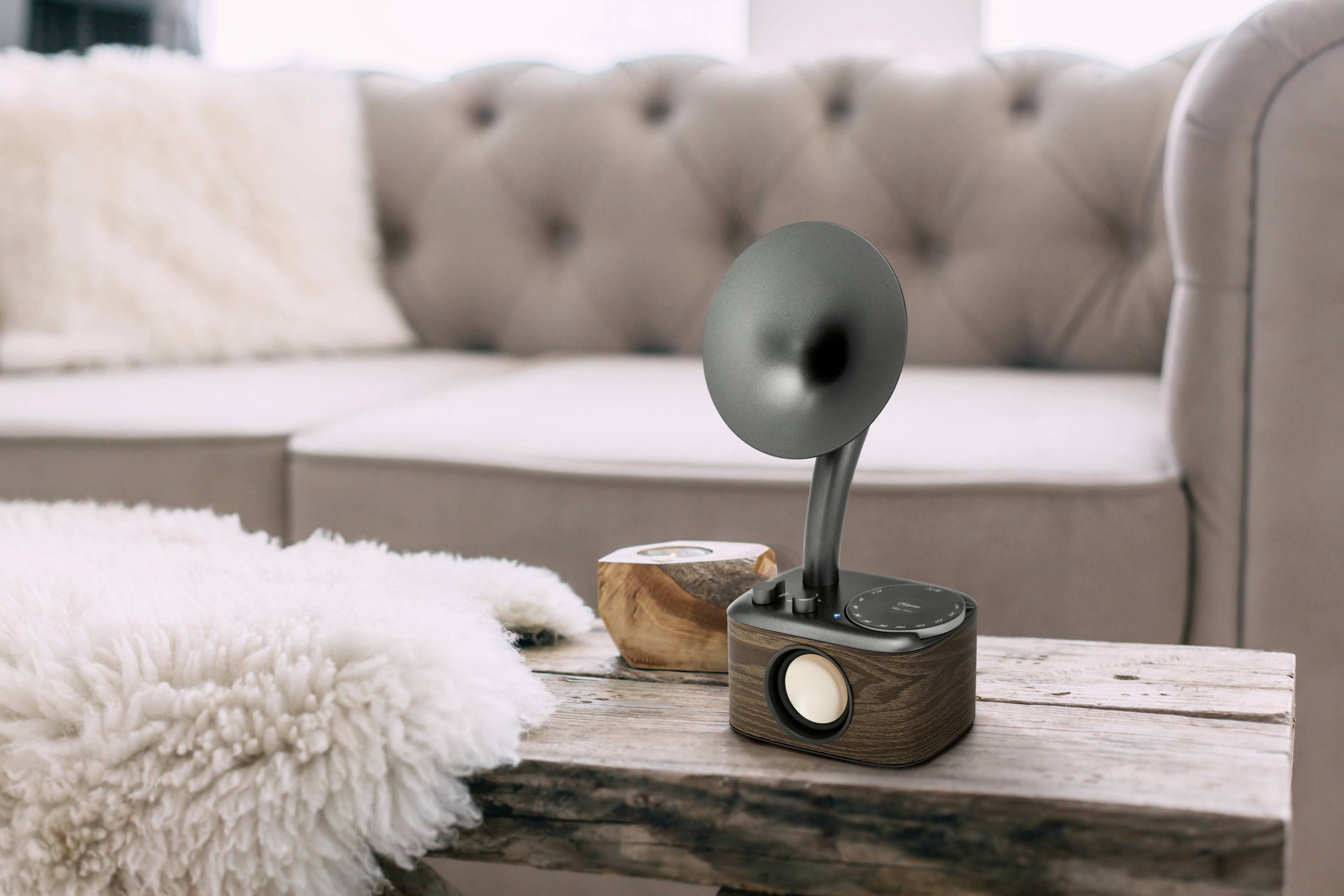 Ein Retro-Radio mit Holzverkleidung und einem schwarzen Lautsprechertrichter steht auf einem Tisch vor einem beigen Sofa mit Kissen.