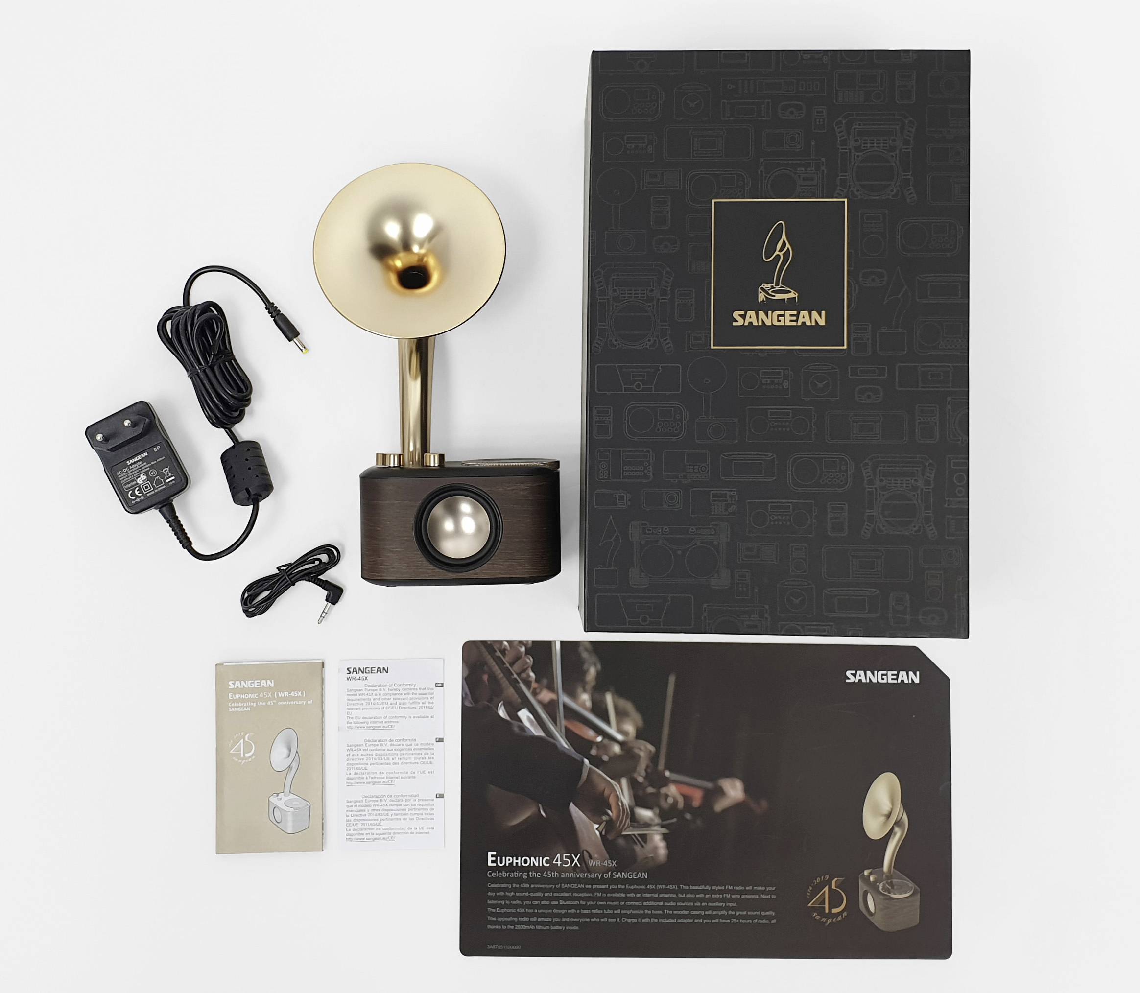 Ein Retro-Radio mit goldener Lautsprechertrichter, daneben Verpackung, Netzteil und Anleitungen. Markennamen 'Sangean'. Atmosphärisches Design.