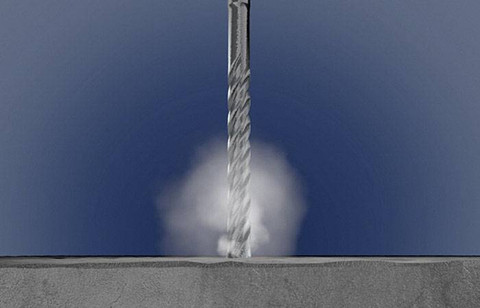 Bohrer durchdringt graue Betonoberfläche, erzeugt Staubwolke.