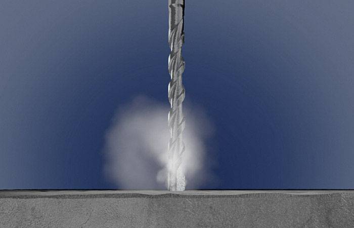Bohrer dringt in Betonplatte ein, Staub wirbelt auf. Fokus auf den Bohrprozess und Materialdurchdringung.