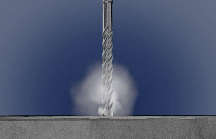Ein Bohrer dringt mit Staubentwicklung in eine graue Betonoberfläche ein, dargestellt vor einem blauen Hintergrund.