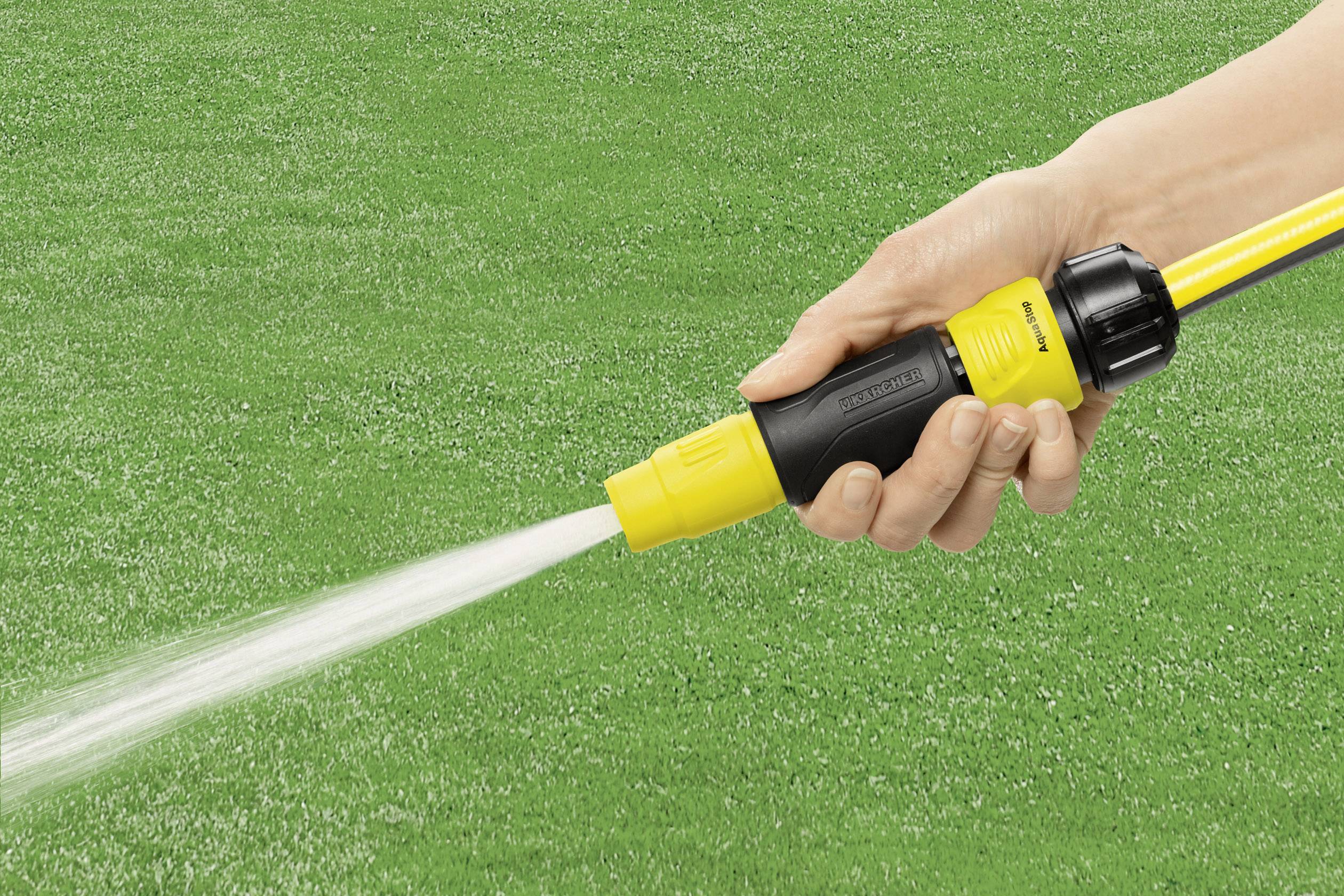 Eine Hand hält einen Gartenschlauch mit Sprühdüse, aus der Wasser auf einen grünen Rasen gespritzt wird.