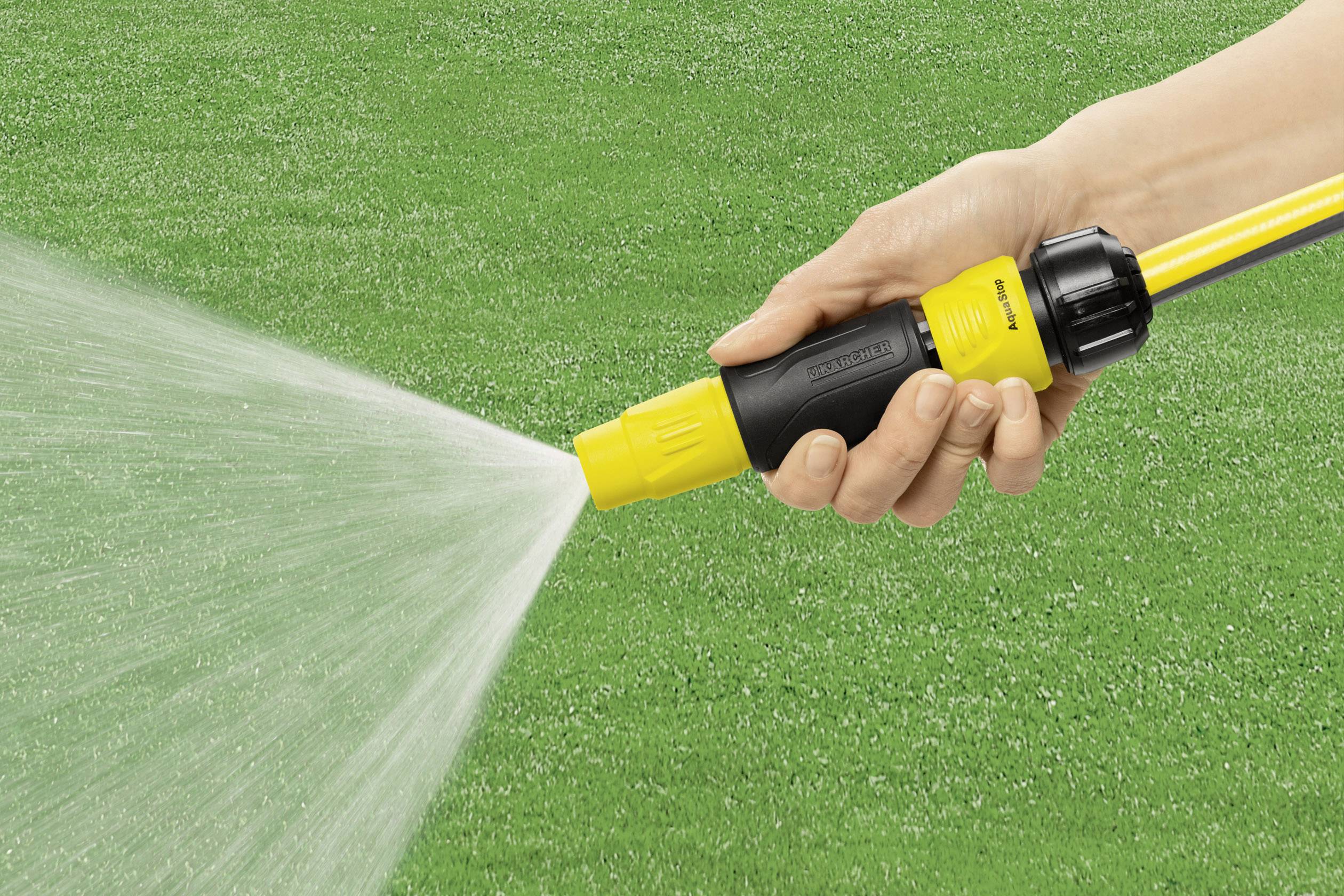 Eine Hand hält eine Gartenschlauchdüse, die Wasser auf einen grünen Rasen sprüht.