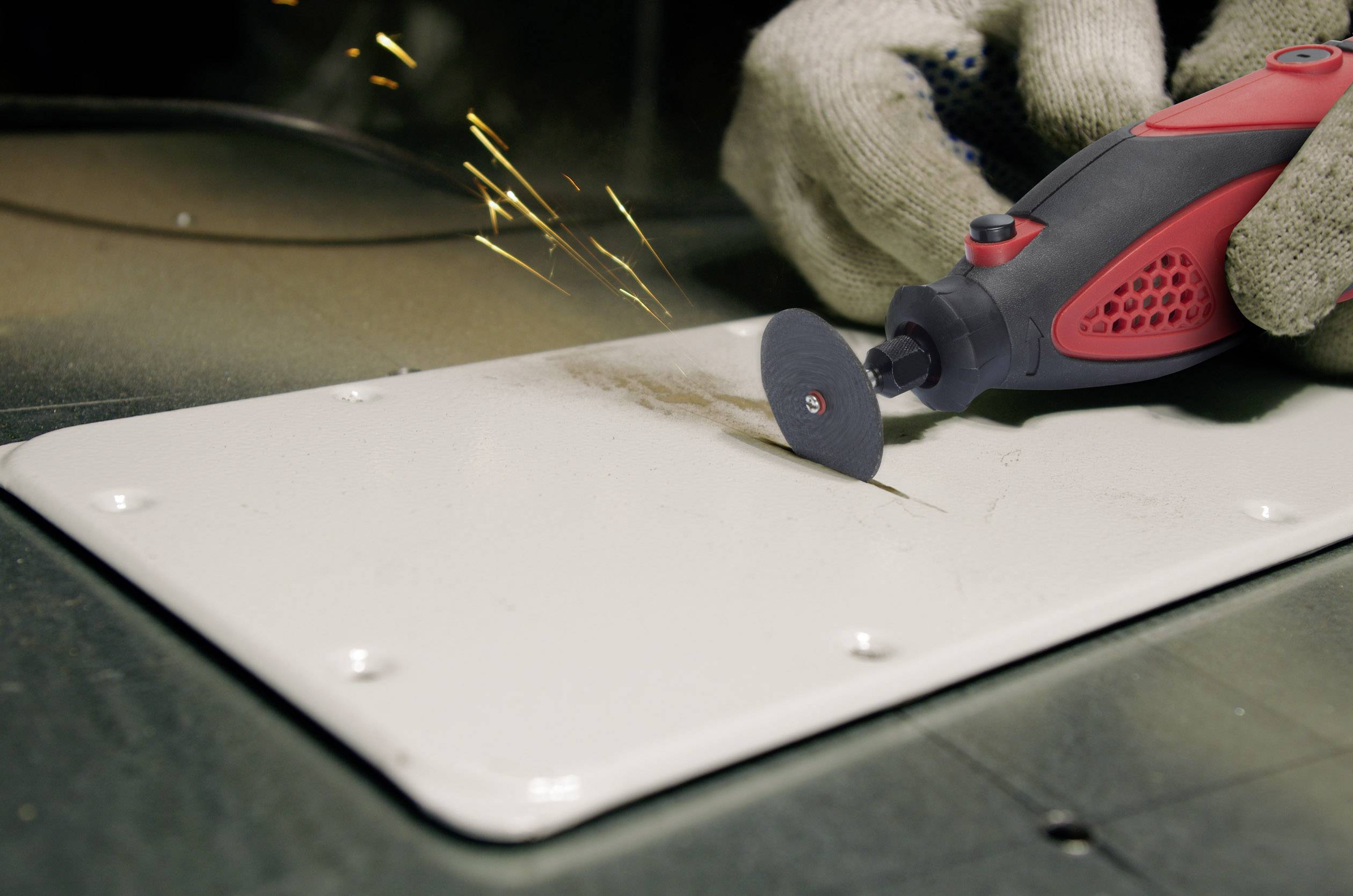 Eine Person nutzt ein rot-schwarzes Handwerkzeug mit Schleifscheibe, um Metall zu bearbeiten. Es sprühen Funken.