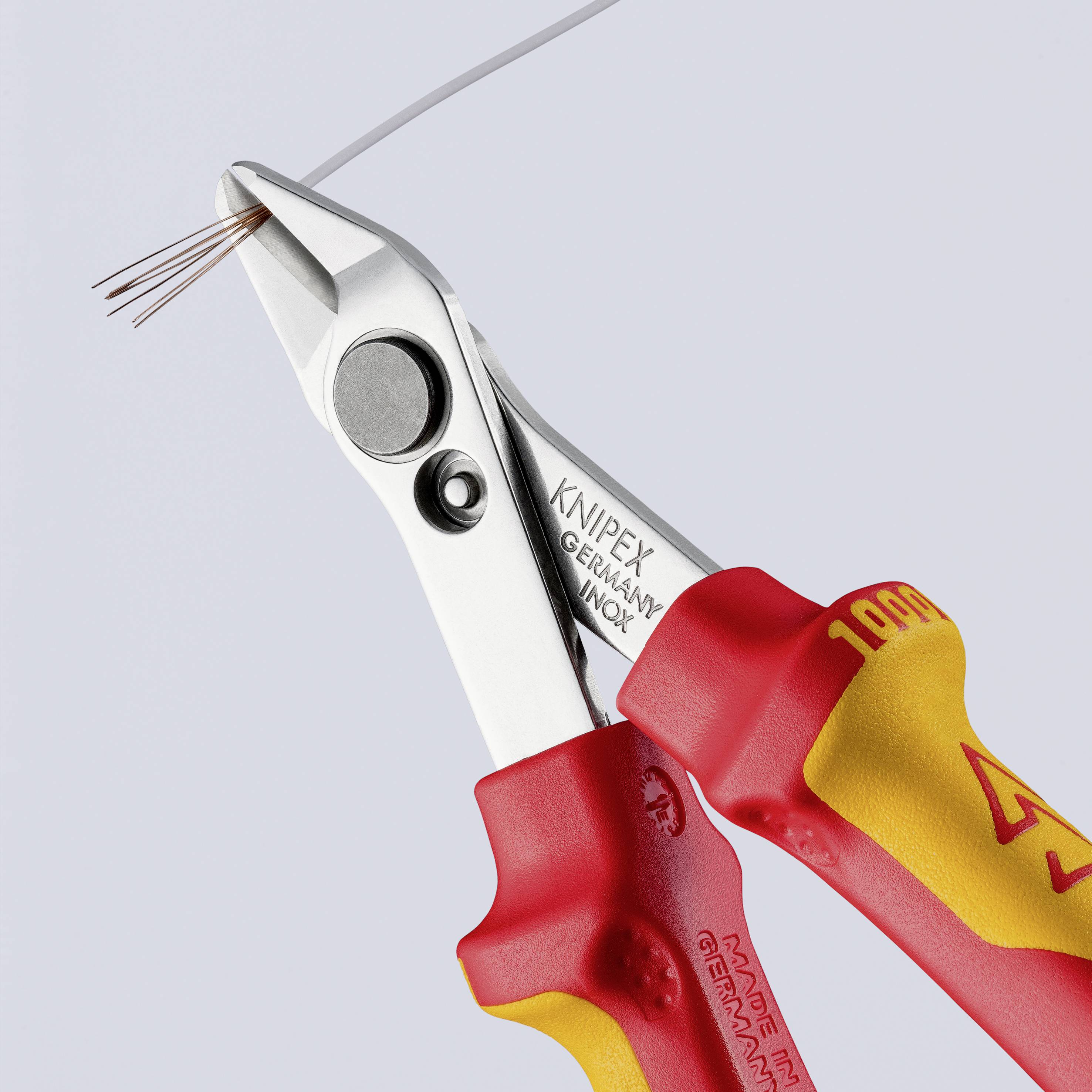 Eine rote Zange von Knipex schneidet ein silbernes Kabel ab. Sie hat ergonomische Griffe und wird in Deutschland hergestellt.