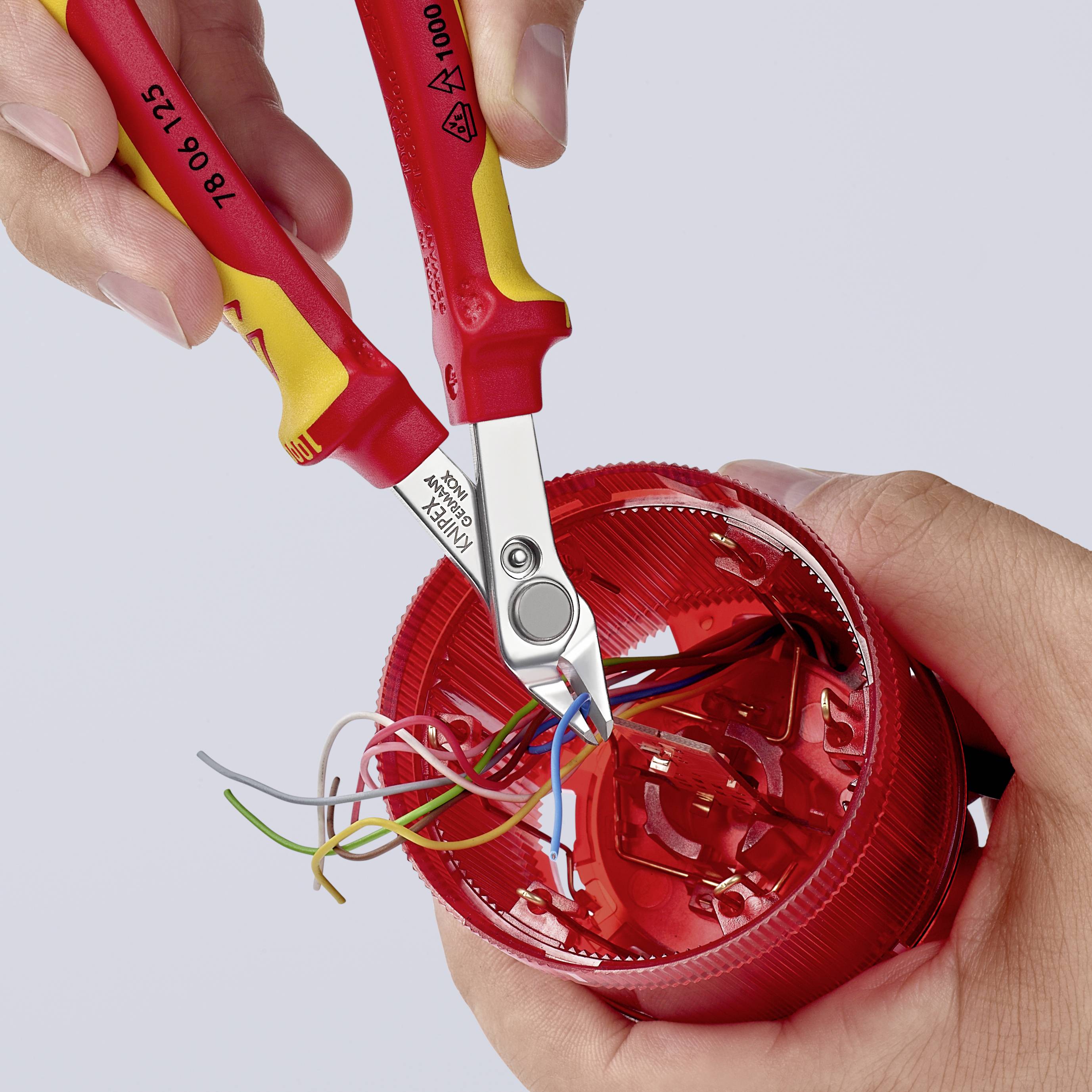 Zwei Hände verwenden einen Seitenschneider, um bunte Kabel aus einem roten, runden Kunststoffteil zu entfernen.