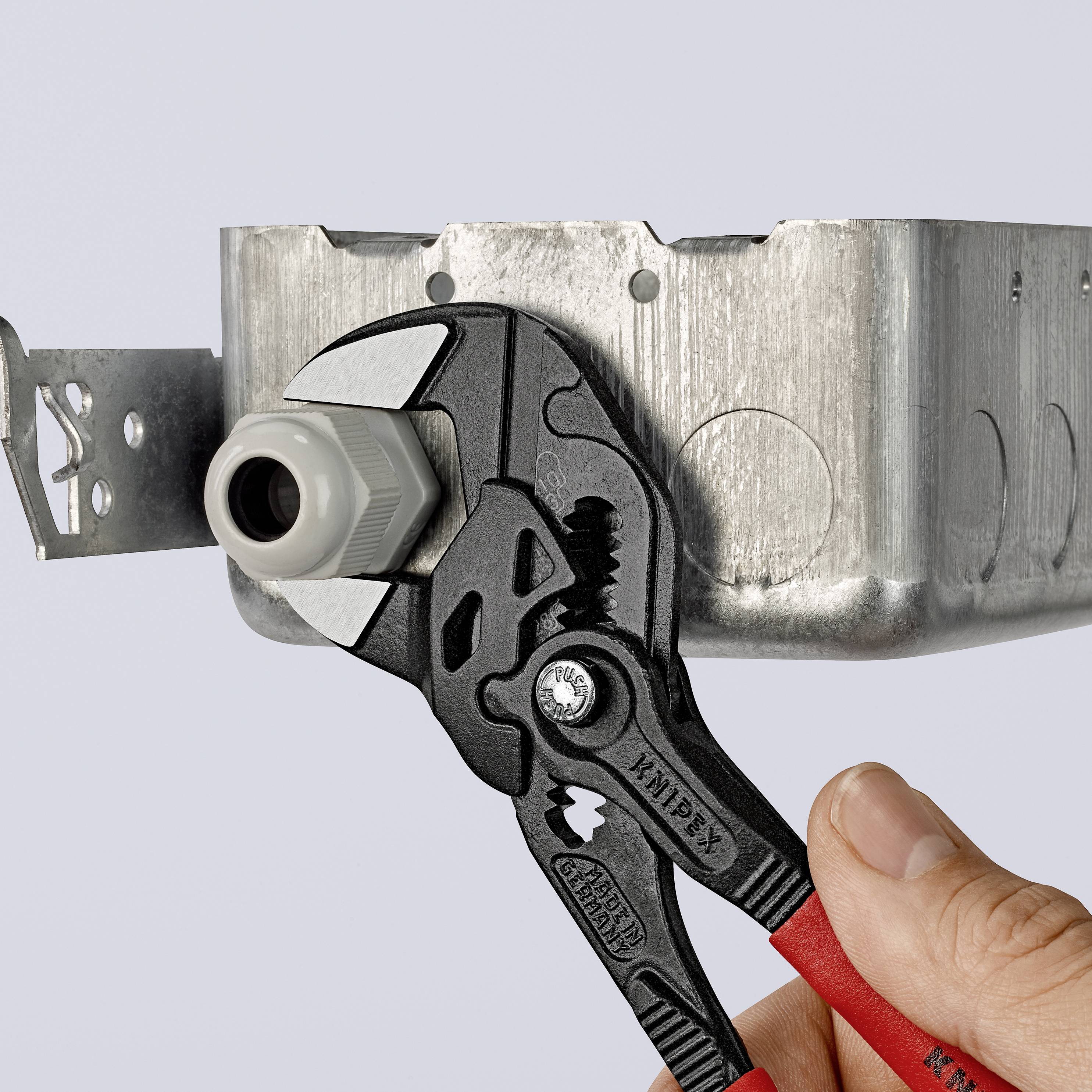 Eine Hand hält eine Zange, die ein Metallstück in einem elektrischen Anschlusskasten befestigt.