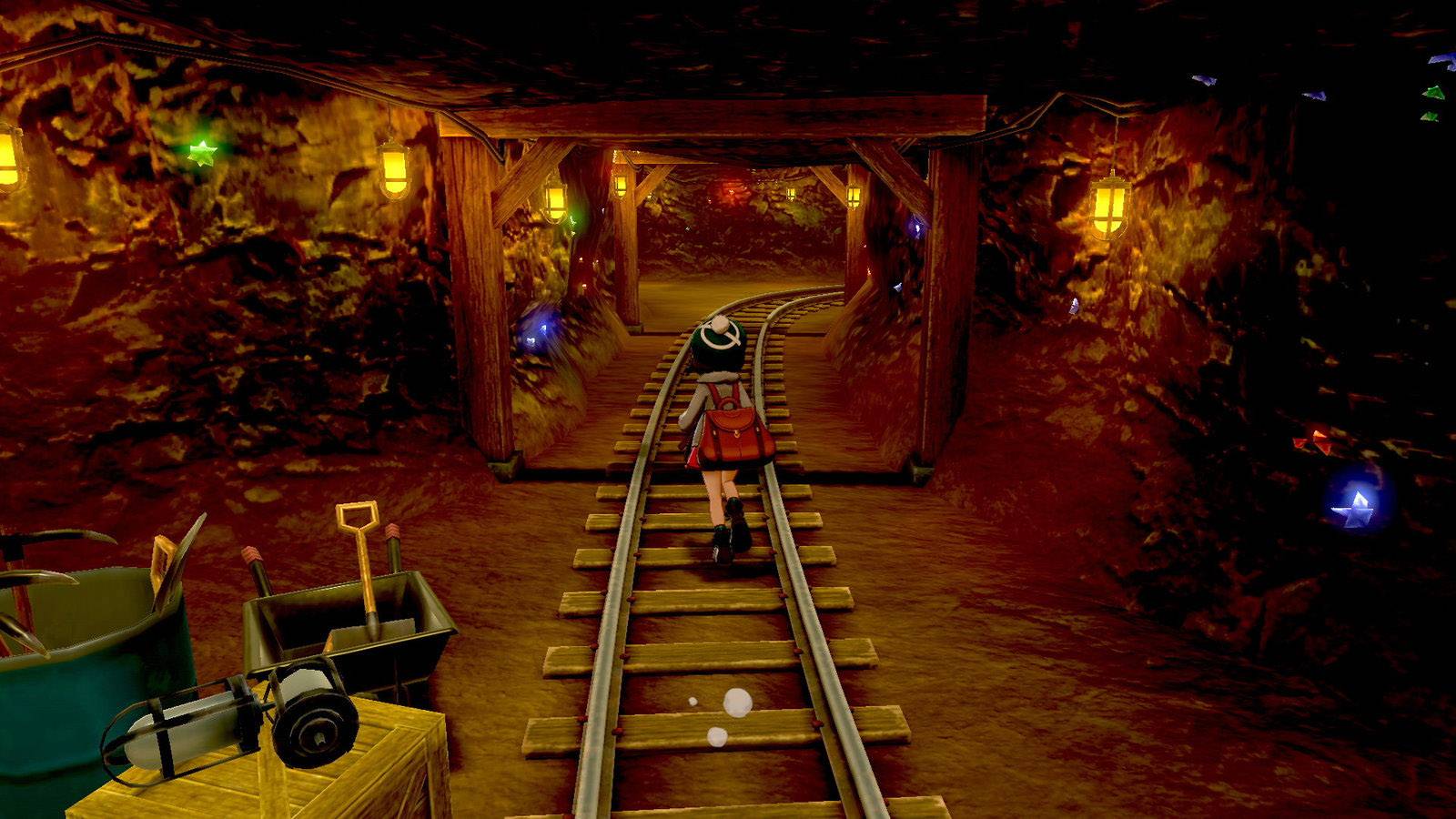 Eine Person in einem Bergwerkstollen geht auf Schienen. Der Tunnel ist mit Lampen beleuchtet. Rechts stehen Werkzeuge in einem Korb.