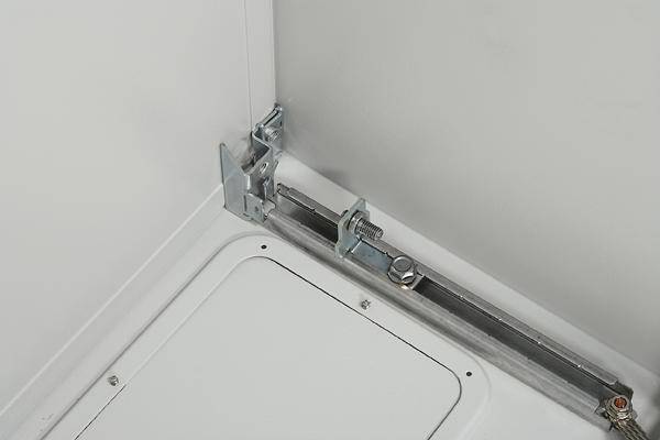 Ein Metallscharnier befestigt eine weiße Tür an einer Metallplatte. Schrauben und ein Bolzenmechanismus sind sichtbar.