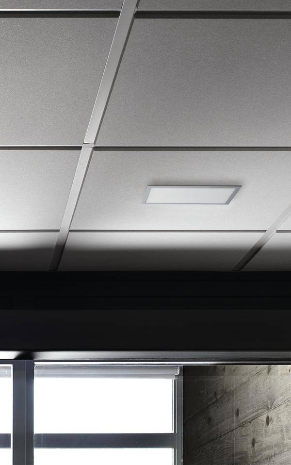 Decke mit quadratischen weißen Paneelen und einem rechteckigen LED-Licht in einem modernen Raum mit Holzwand und Fenster.