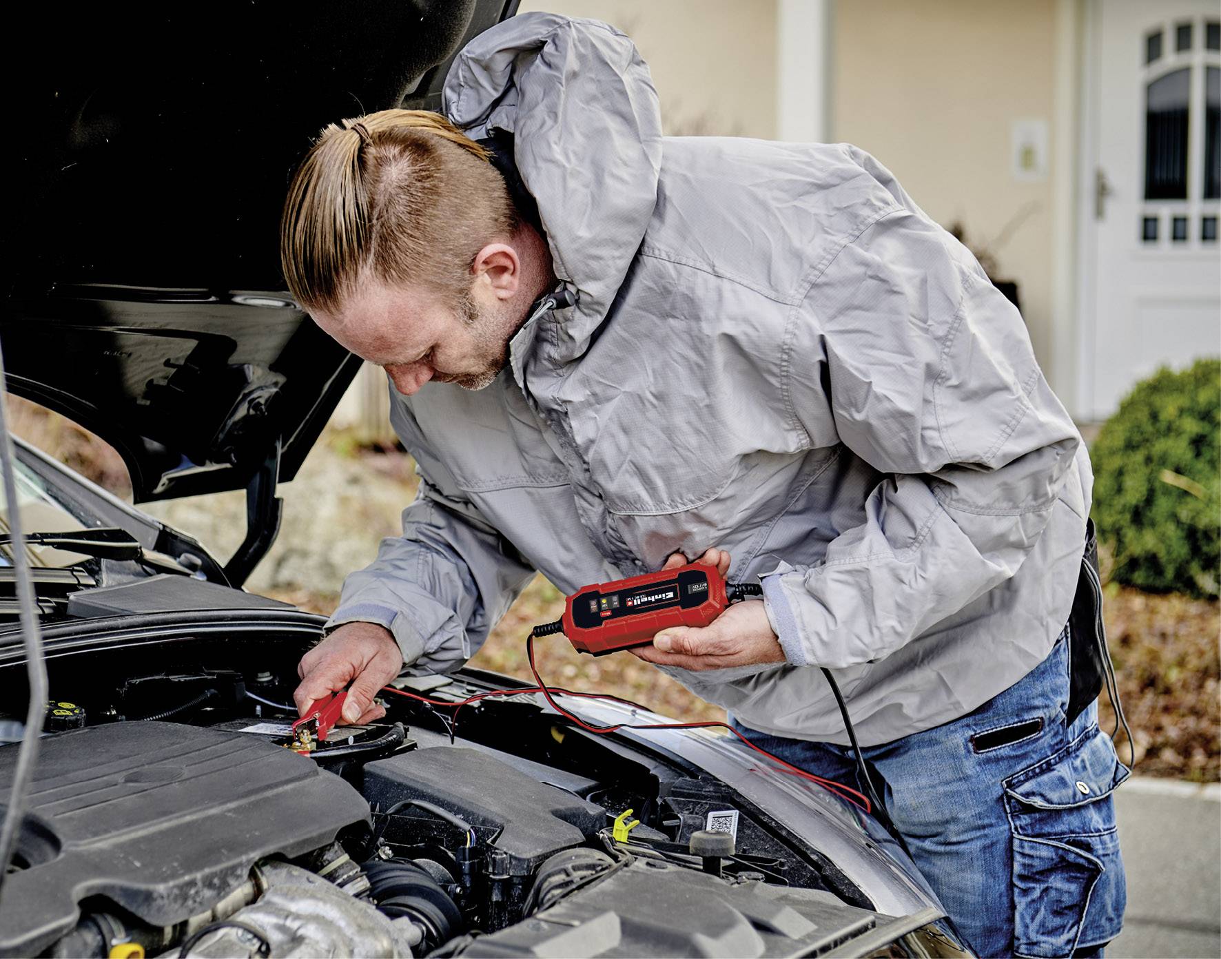Ein Mann überprüft mit einem digitalen Messgerät den Motor eines Autos.