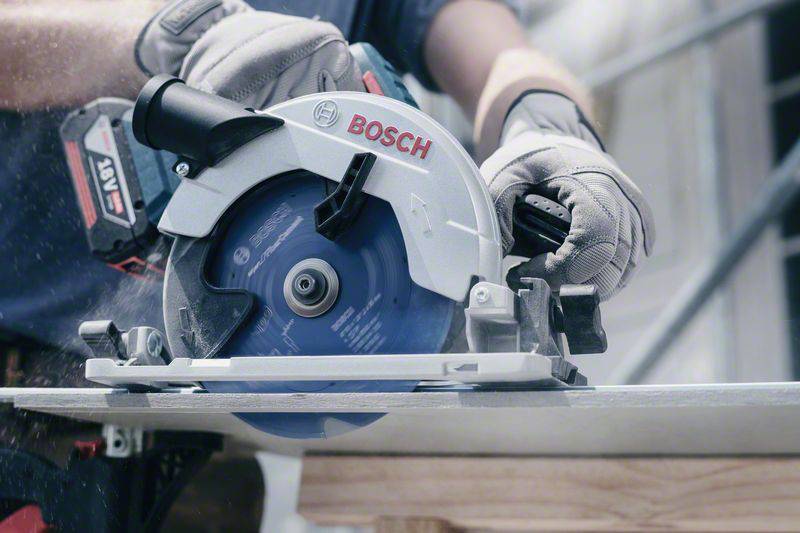 Person sägt mit einer Handkreissäge ein Brett. Die Säge ist von der Marke Bosch. Schutzkleidung wird getragen.