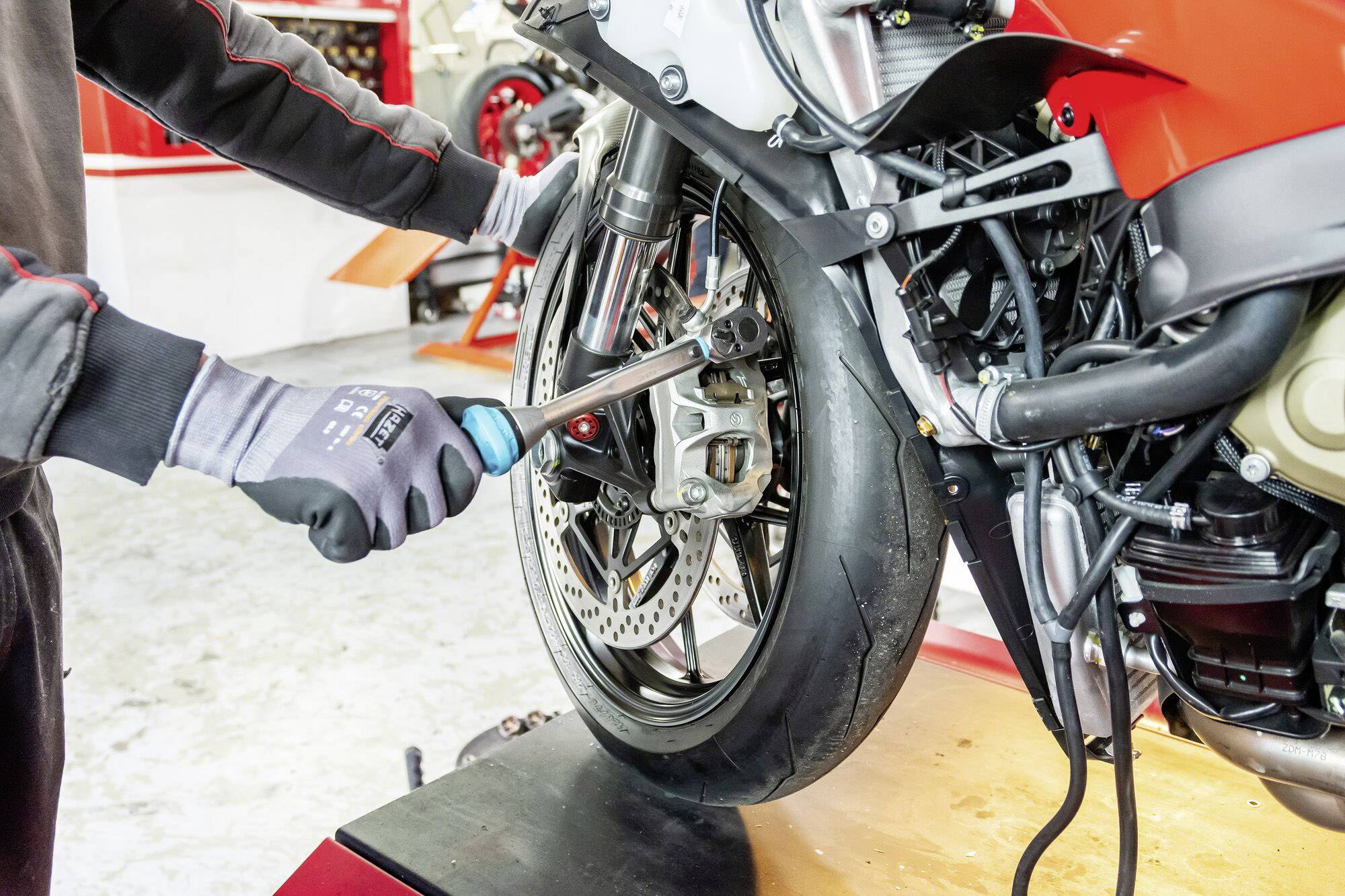 Eine Person repariert das Vorderrad eines Motorrads auf einem Werkstatttisch, indem sie mit einem Schraubenschlüssel daran arbeitet.